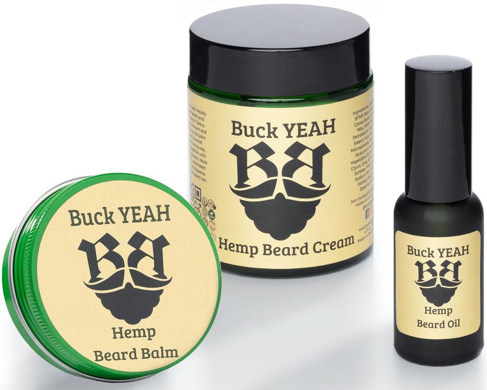 A trio of Buck YEAH brand hemp beard care products: a round tin of Hemp Beard Balm, a large glass jar of Hemp Beard Cream, and a small dropper bottle of Hemp Beard Oil. Each product features a cream-colored label with a black logo of a stylized bearded face.