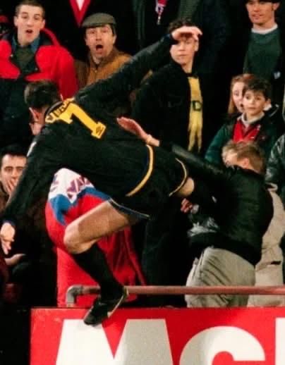 Eric Cantona flying through the air with legs and feet horizontal, heading towards racially abusive Crystal Palace fan.