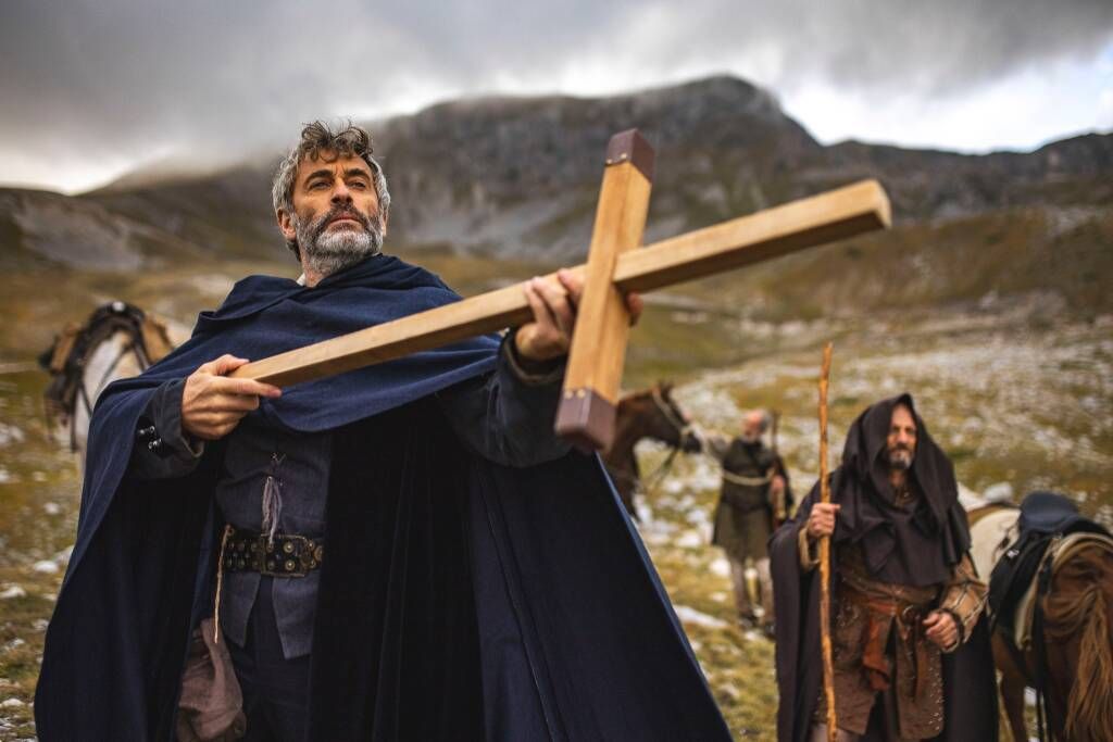 Scena del docufilm diretto da Luca Cococcetta che racconta l’impresa storica di Francesco De Marchi. La scena mostra il protagonista in piedi con una croce in mano immerso in un panorama montano.