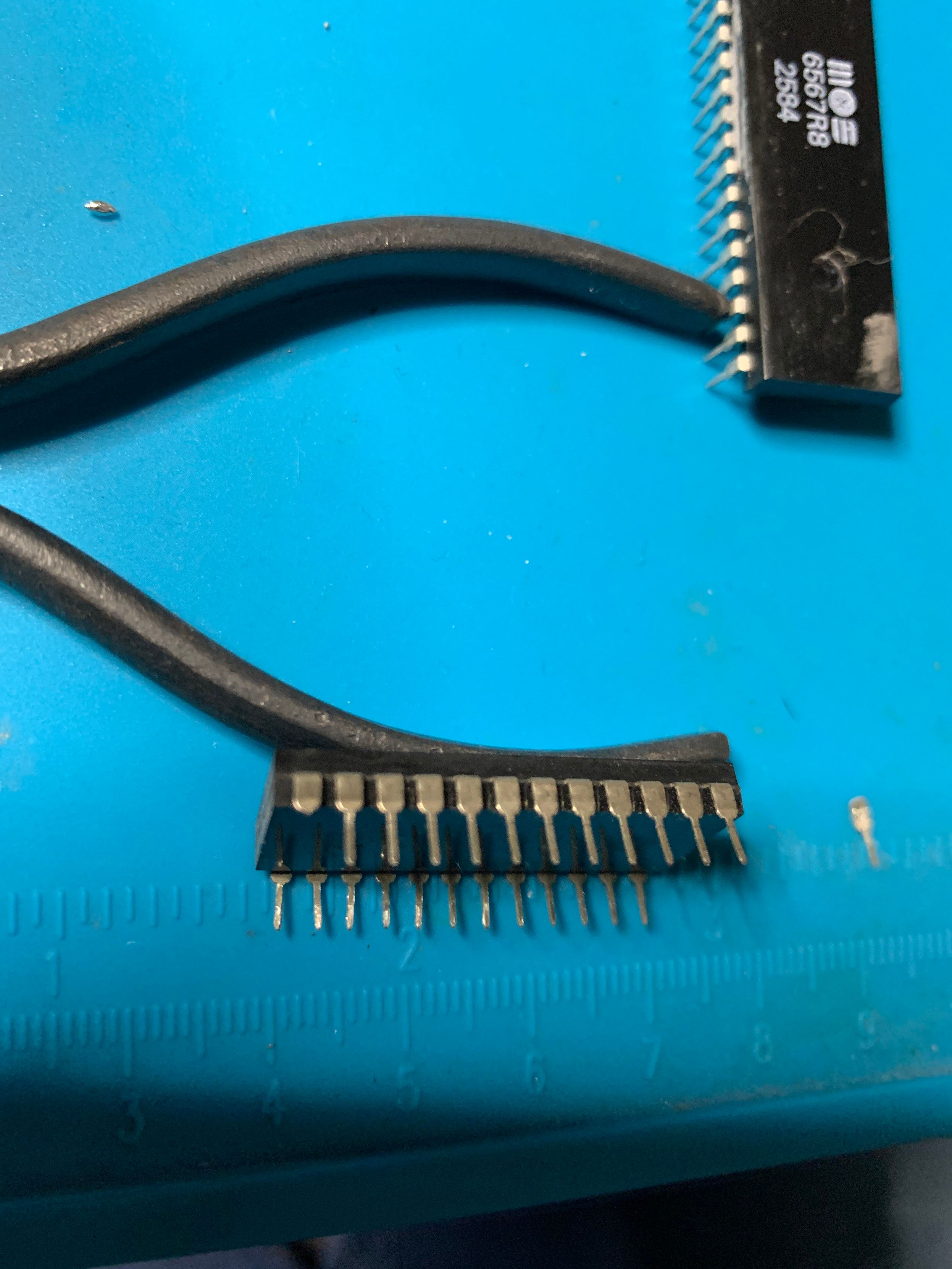 Profile view of the right side of the BASIC ROM removed from its socket showing a missing pin. A replacement pin sits to the right on a blue work mat