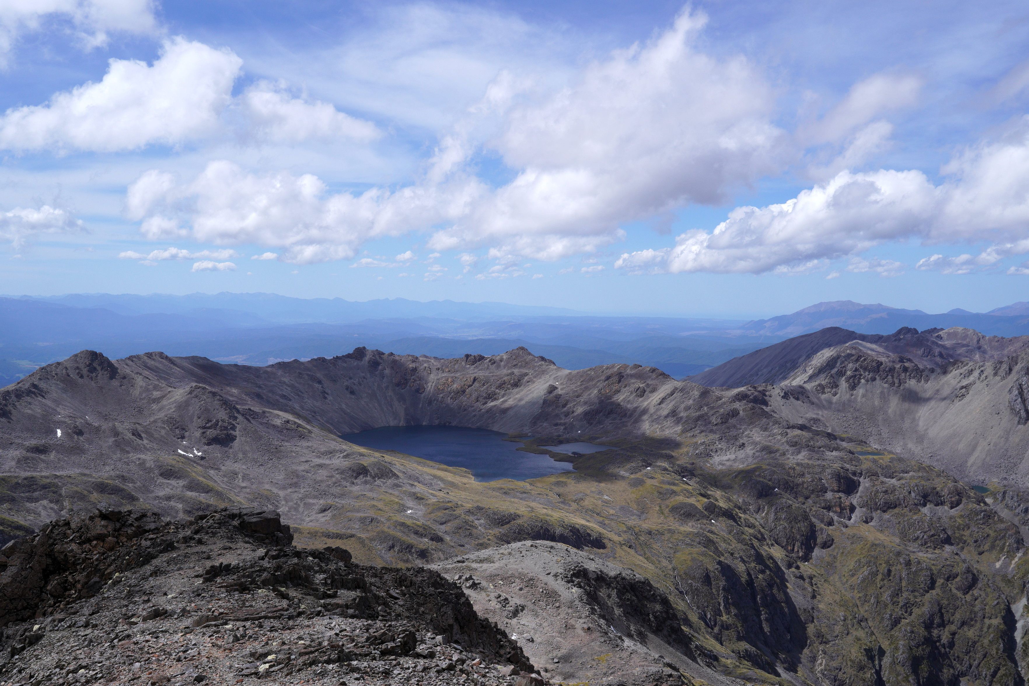 Angelus Lake prominent in the centre of this photo on a pretty windy, partly cloudy day with lots of sunshine. Mountains abound. There is a hut which you can barely see on the shores of the lake.