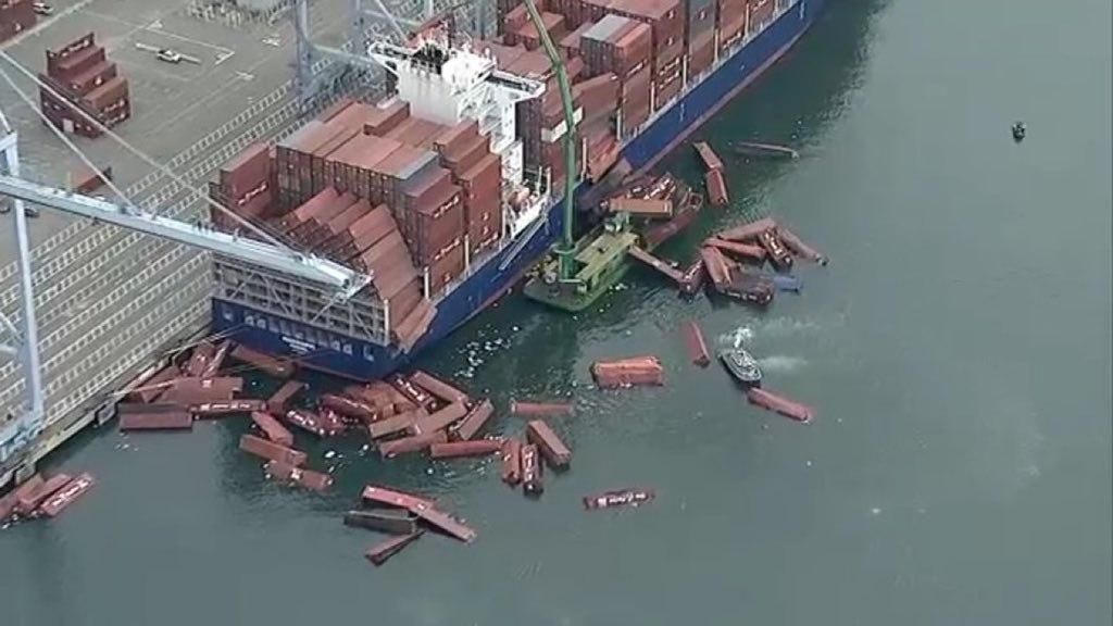 photo of a container ship at port. multiple containet stacks collapsed and many containers are floating in the water