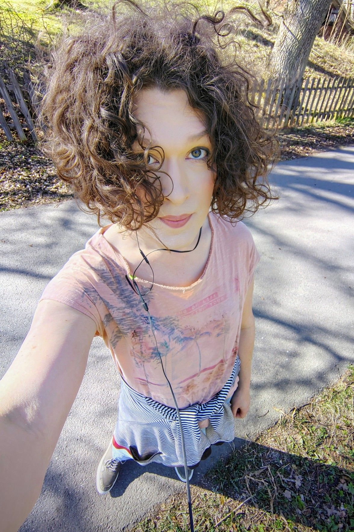 me, selfie with a wide lens from above, I'm looking up at the camera, wearing a summery orange top with short sleeves and an abstract print, a white and black striped hoodie tied around my waist. it is sunny and early spring