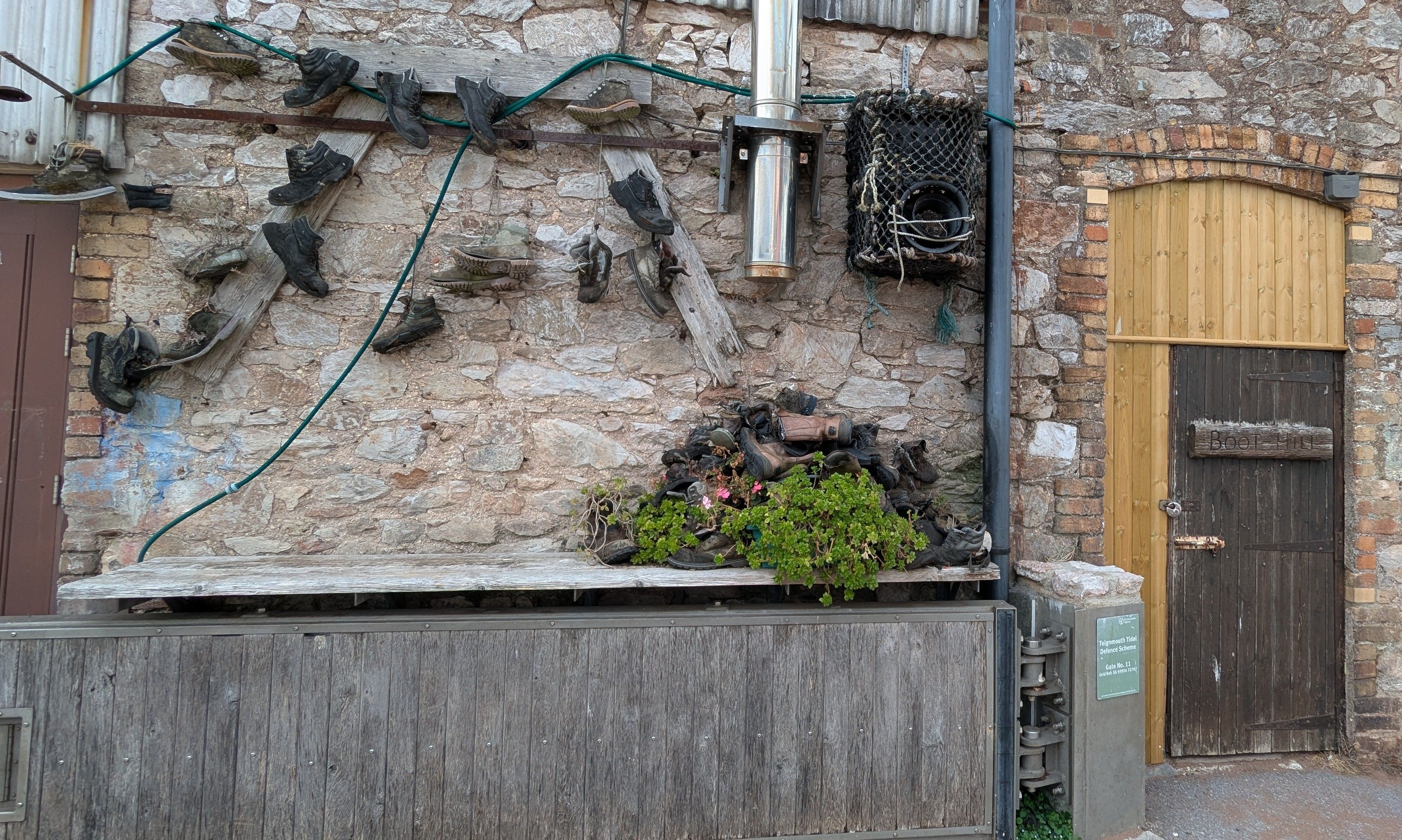 This is a building wall with a number of people's boots attached to it and door to the right with a sign on it that says boot hill. It's not a hill. It's a key that leads to the quey and the Riverside.  Below the boots there is a floodgate that can be closed if necessary. 

The brickwork in the wall is kind of messy and looks like there are many people who have been involved with building and making this wall over the years