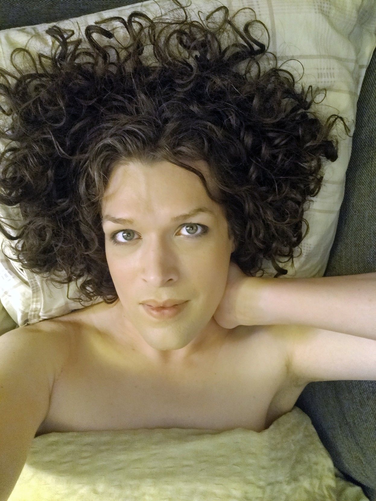 me on the sofa bed on my back under the green blanket, my curly dark hair spread out around my head, smiling slightly, holding my left hand on my neck.