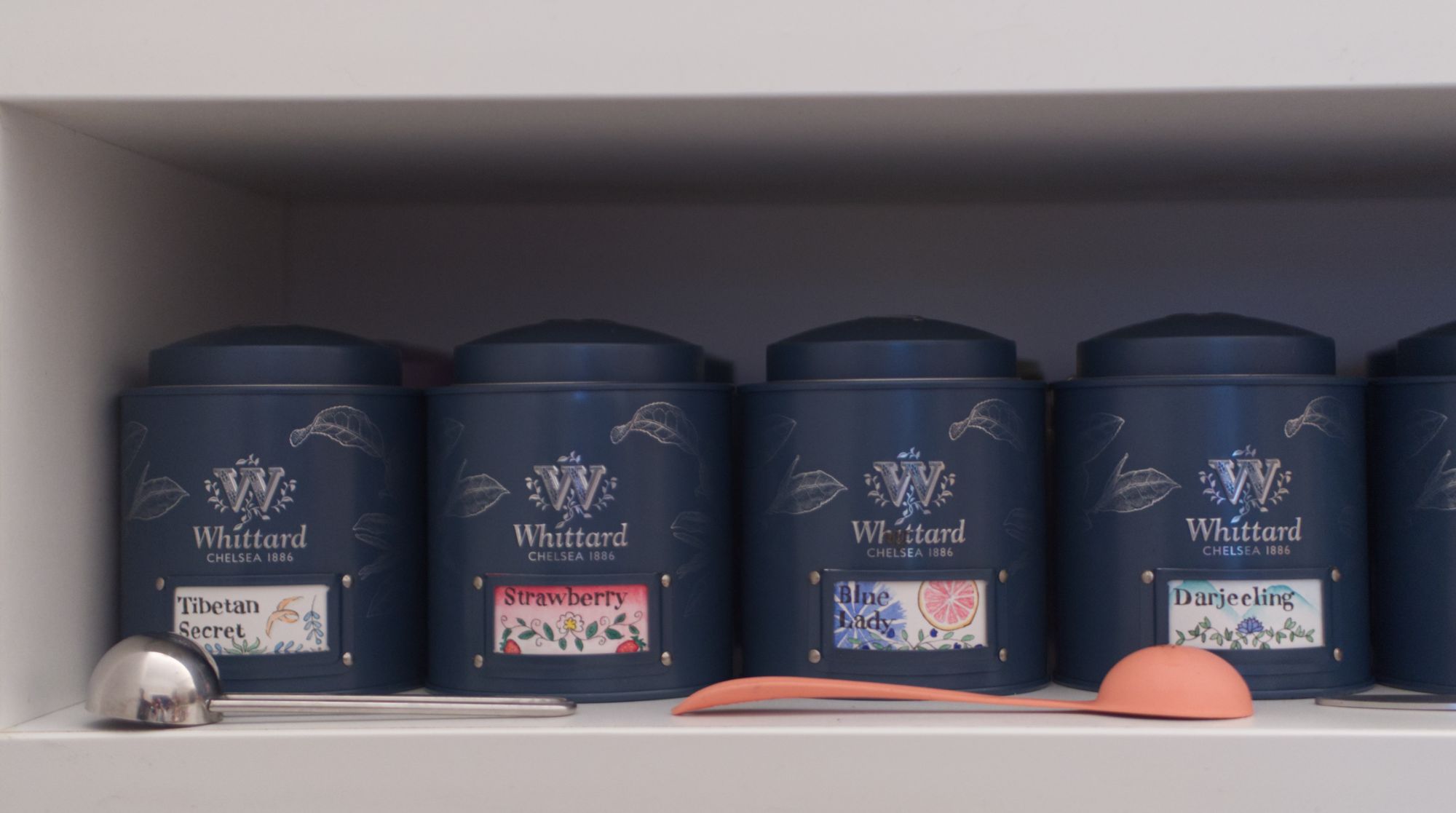 4 Teal coloured stout tea caddies with labels that read: Tibetan Secret, Strawberry, Blue Lady, and Darjeeling. 