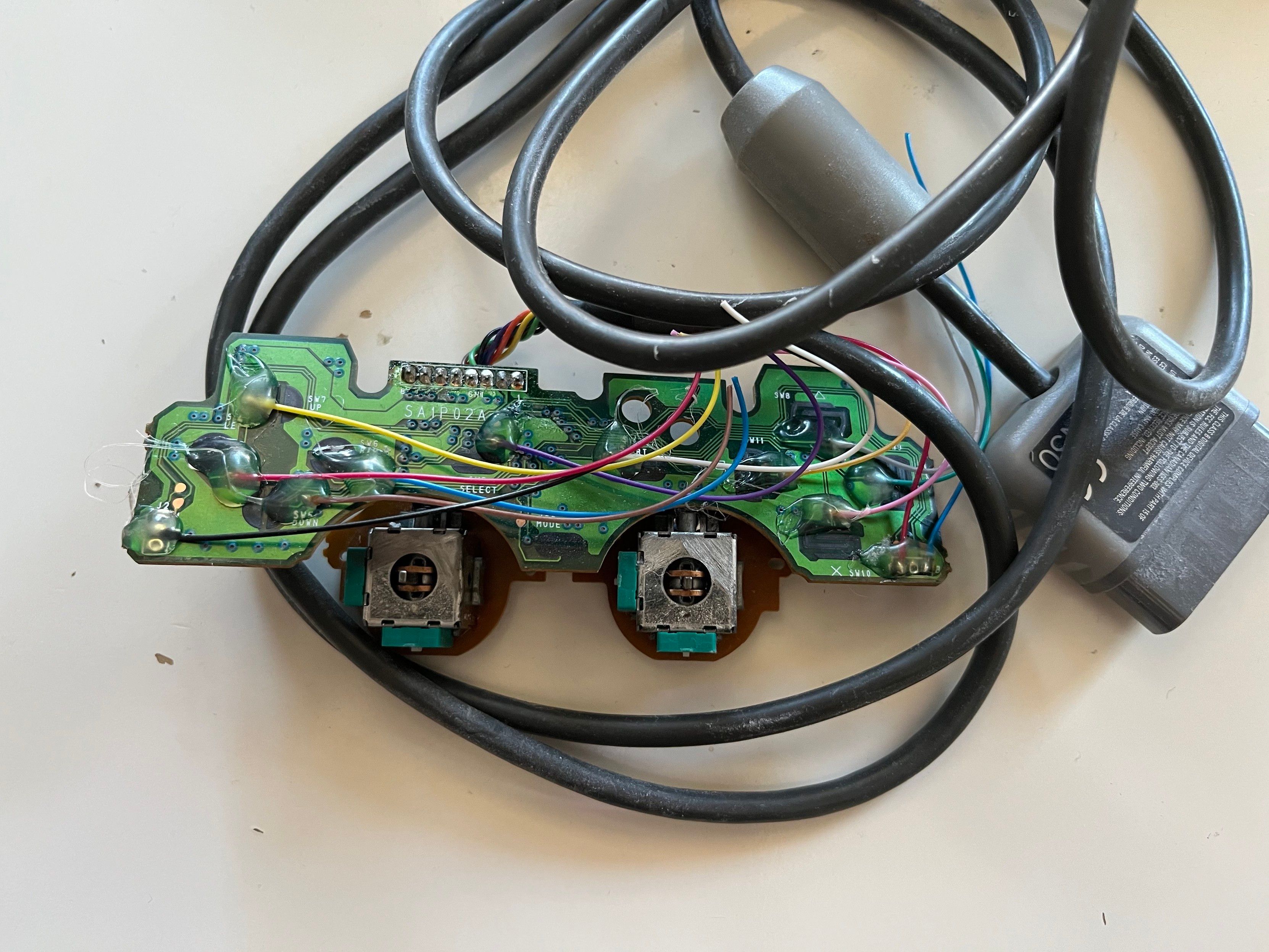 Photo of the boards from a Sony Dual Shock controller for PS1, with wires soldered onto the buttons. 