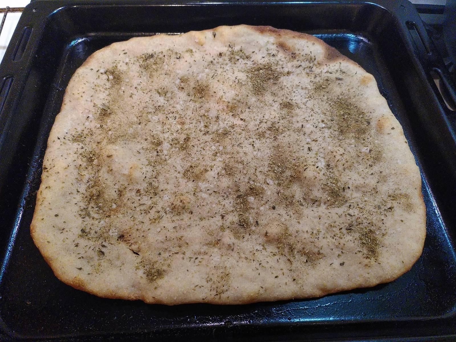 Una schiacciata olio e origano sopra una teglia da forno nera