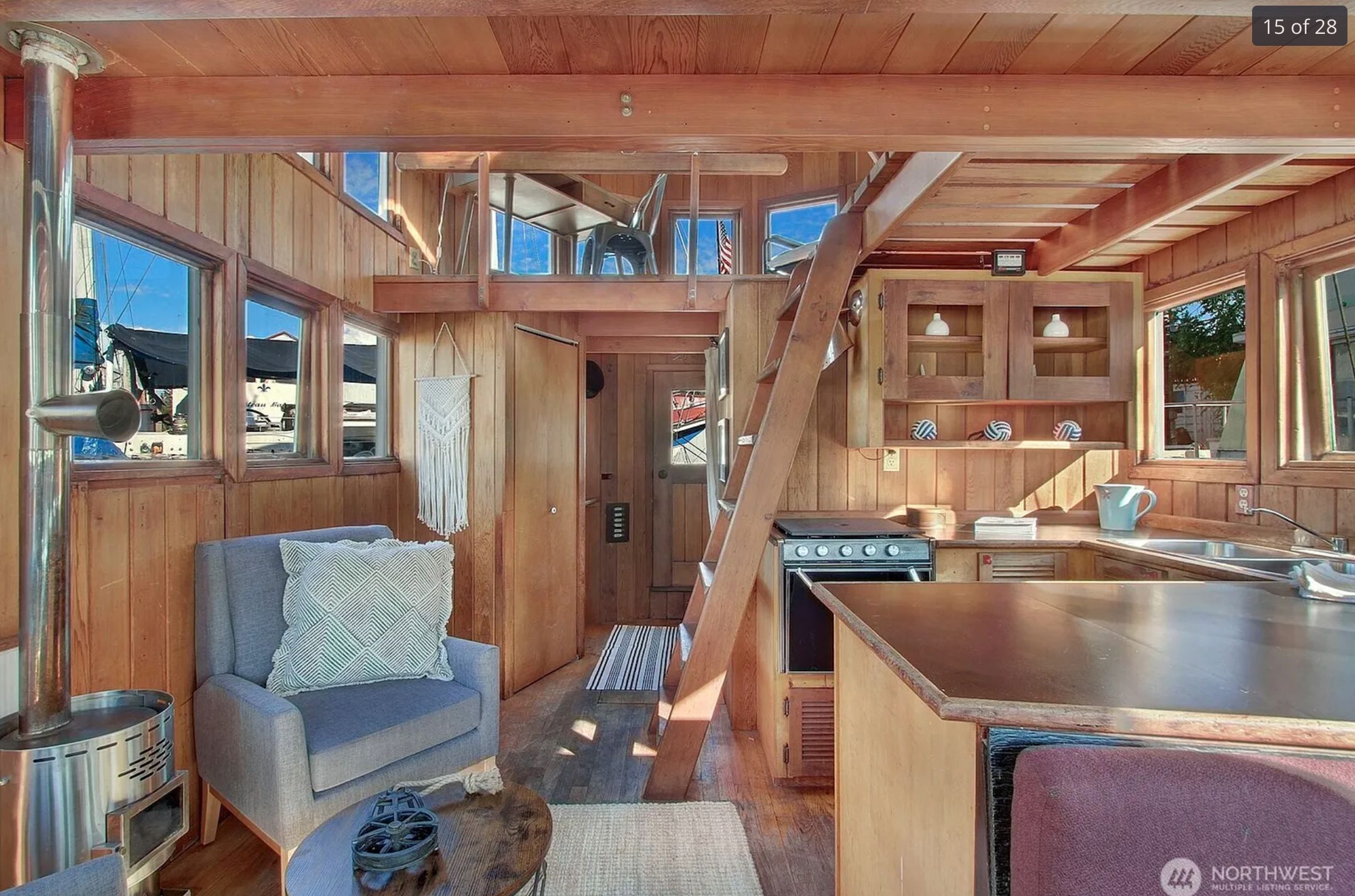 The interior of the house which is entirely clad in cedar wood. It shows the kitchen and a ladder up to the loft, all of which are in the same wood. 