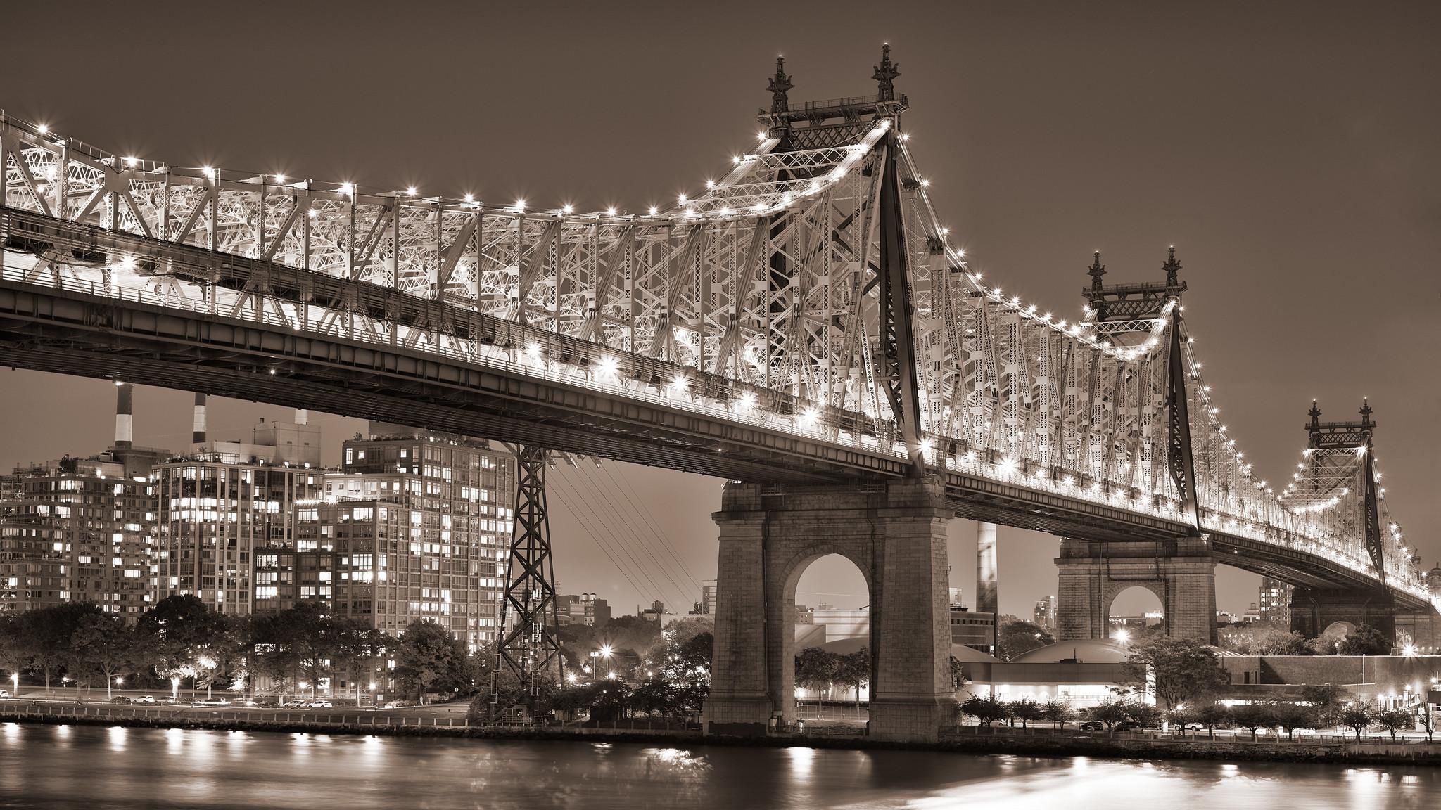 A large cantilever bridge, illuminated along its superstructure, at night.