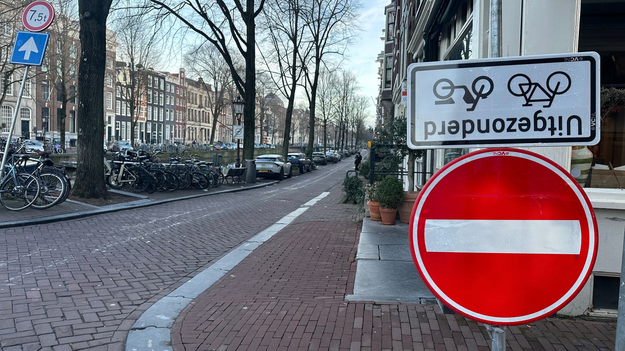 brick street next to a canal with a do not enter sign below an upside down fietsen uitgezonderd sign.