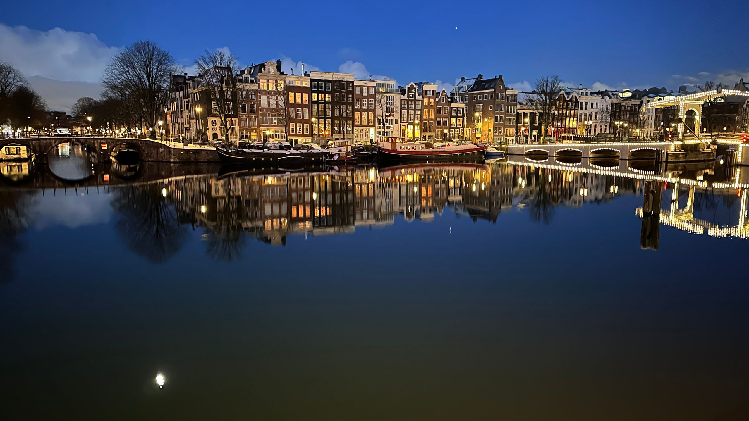 canal houses along a river with an illuminated bridge to the side.  the reflections of the moon and houses are visible in the ripples.