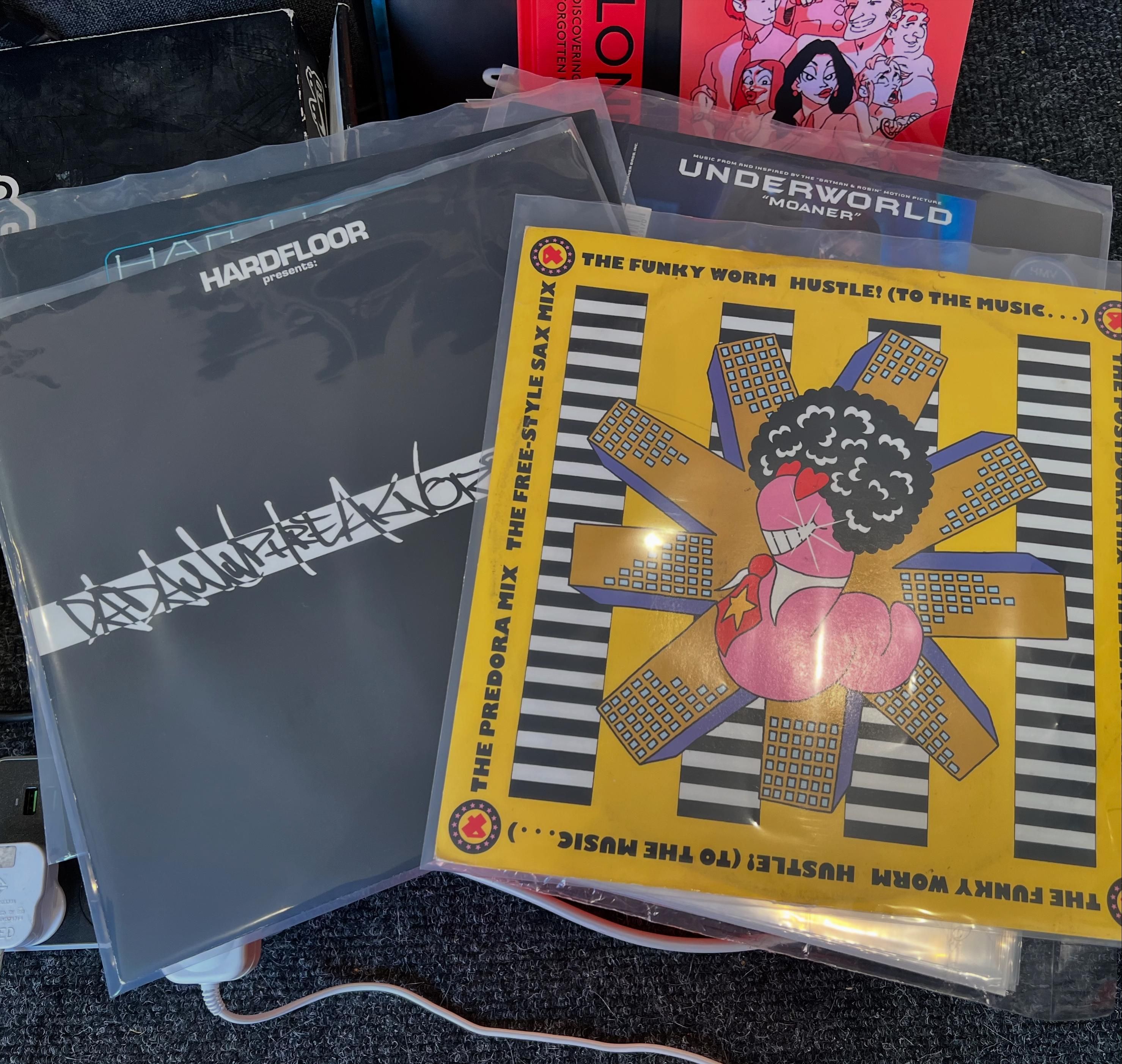 A photo of some 12” records lying on a shoe box. On the left are Hardtrance Acperience andnDadamnphreaknlizphunk? EPs by Hardfloor, and on the right is the import of Underworld’s Moaner and on top of that is Hustle! (To The Music…) by The Funky Worm.
