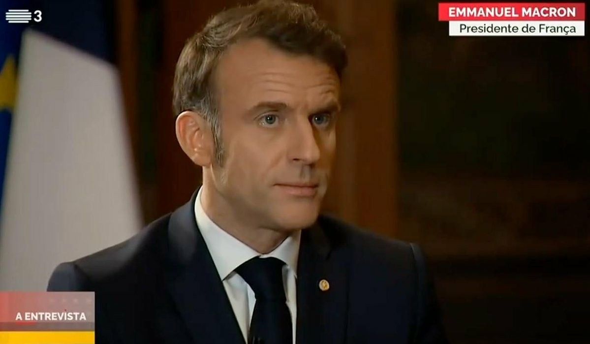 Still of a TV interview with France's President Emmanuel Macron. He is looking to the right of the camera, presumably at the interviewer.
There are television banners at the top right and bottom left of the still.
