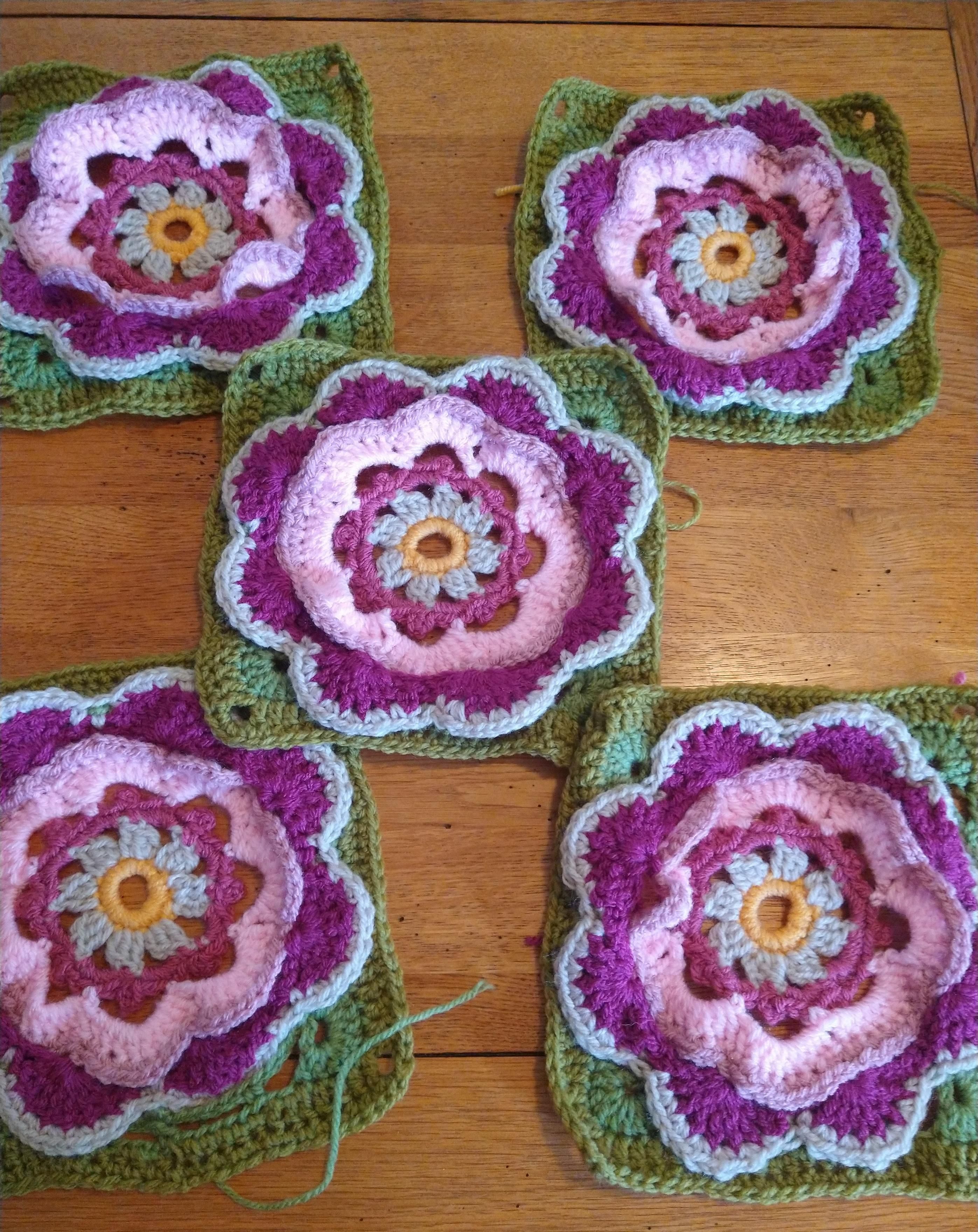 5 Square crochet blocks in greens and pinks each with a flower motif in pink and green 