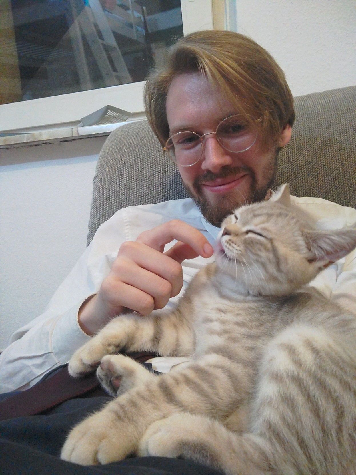 A picture of Erik Uden and his cat playing. The cat is licking Erik Uden's finger