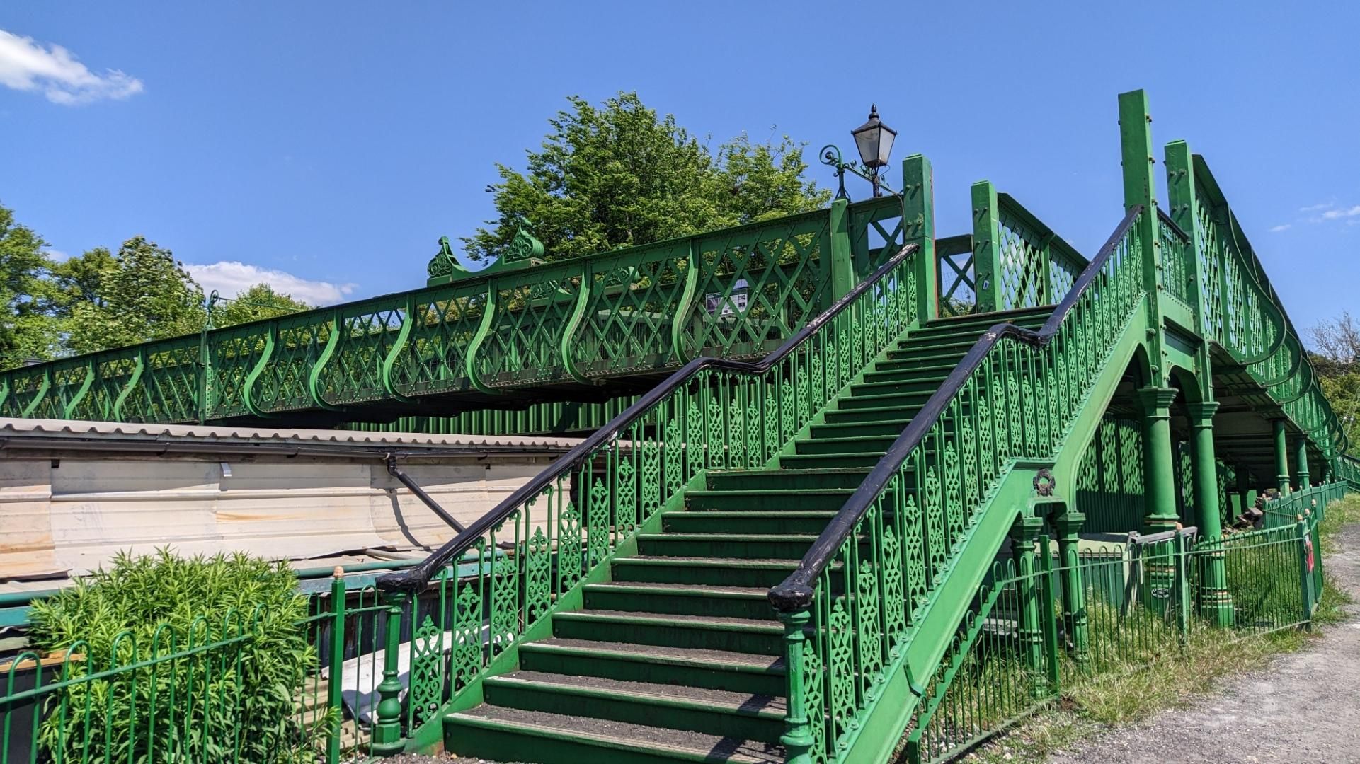 Stairs upwards onto a large green footbridge with decorative siderailings