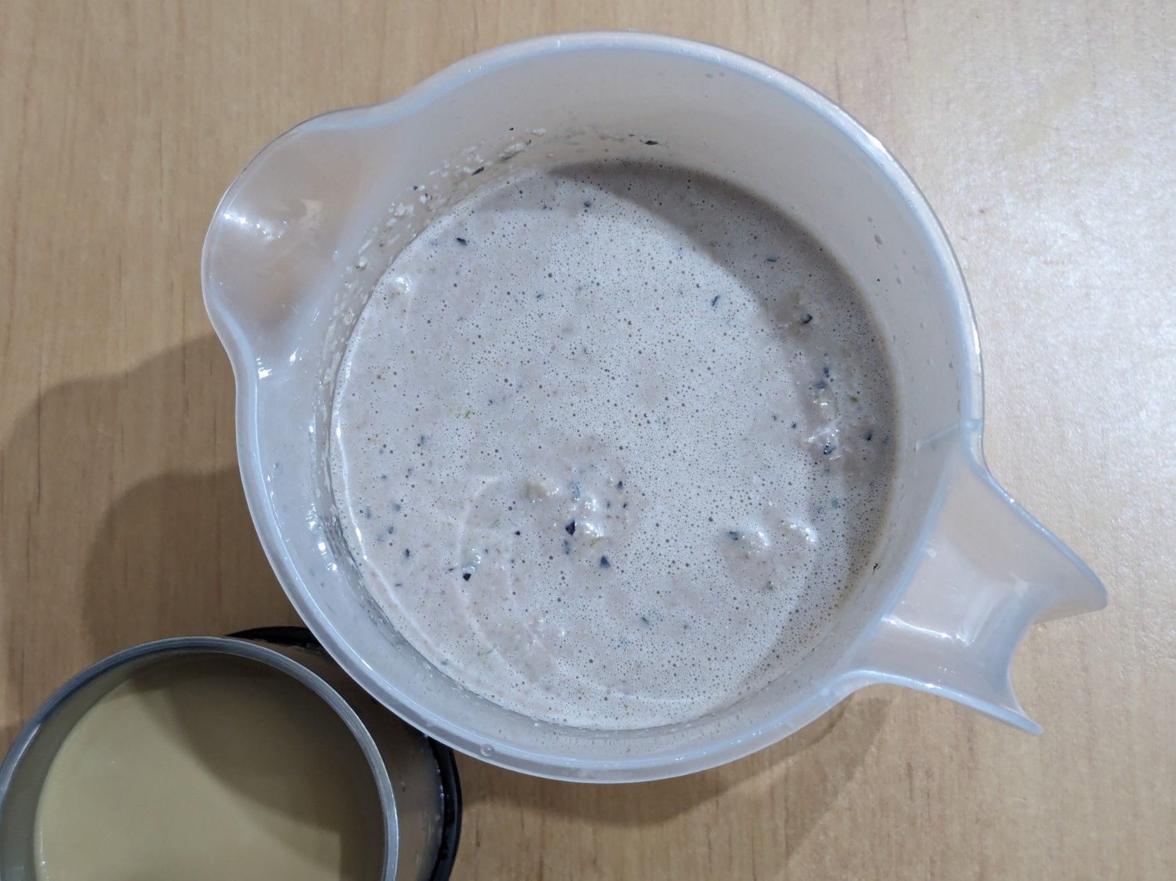 The same jar from previous picture but seen from above, and a metal cup with coffee and milk next to it.