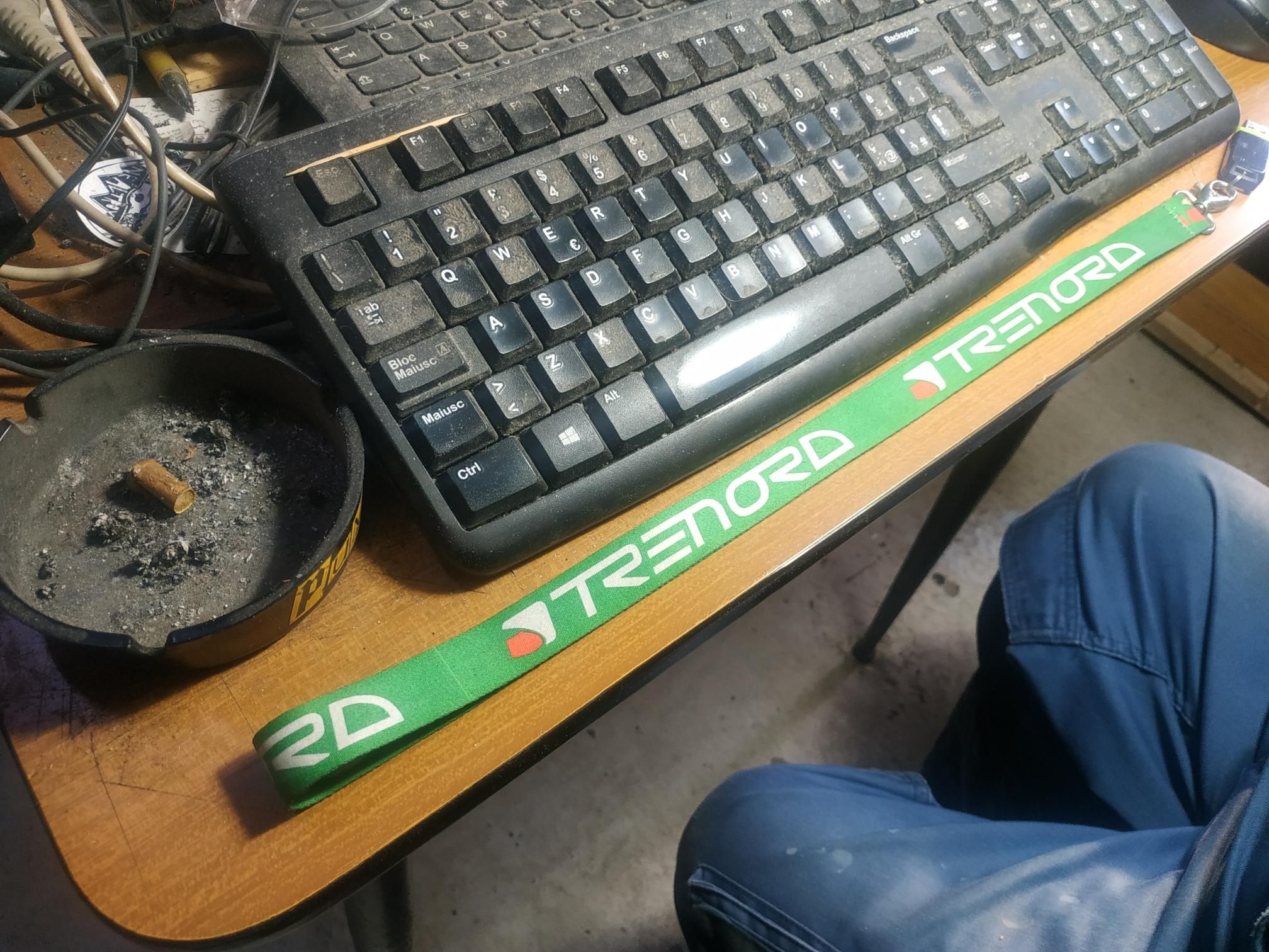 foto di una scrivania con un nastro portachiavi verde di trenord e una tastiera un po' impolverata.