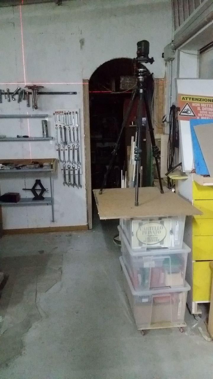 Il livello laser Lidl montato su un cavalletto fotografico Manfrotto 190 XPROB nero, appoggiato sopra un pezzo di MDF di scarto che sta su una pila di tre contenitori trasparenti Ikea Samla da 57×39×28 cm, montati su rotelle.