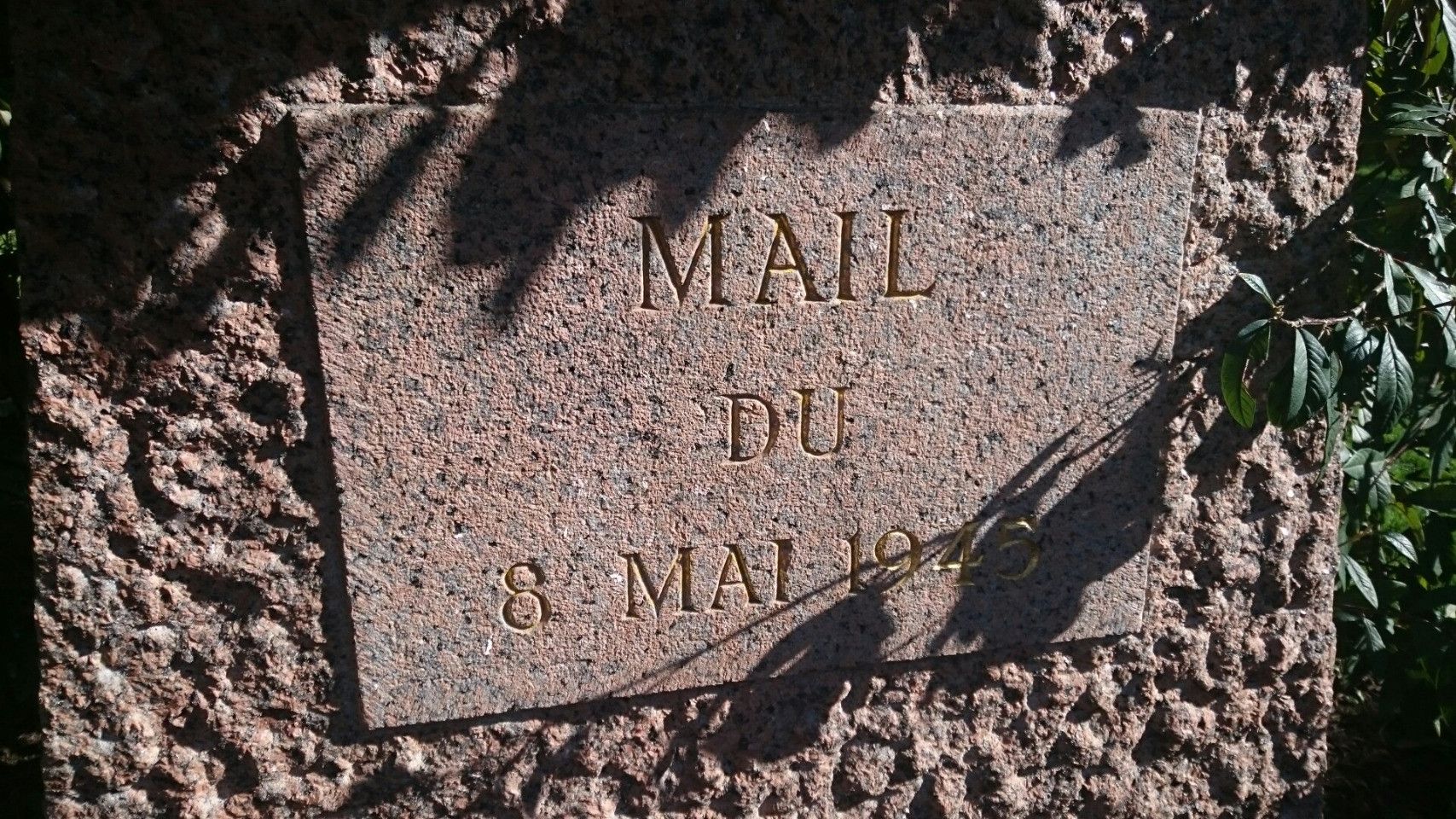 Photo d'une plaque de marbre posée verticalement sur une stelle. Sur la plaque est gravé "Mail du 8 mai 1945” en lettres dorées.