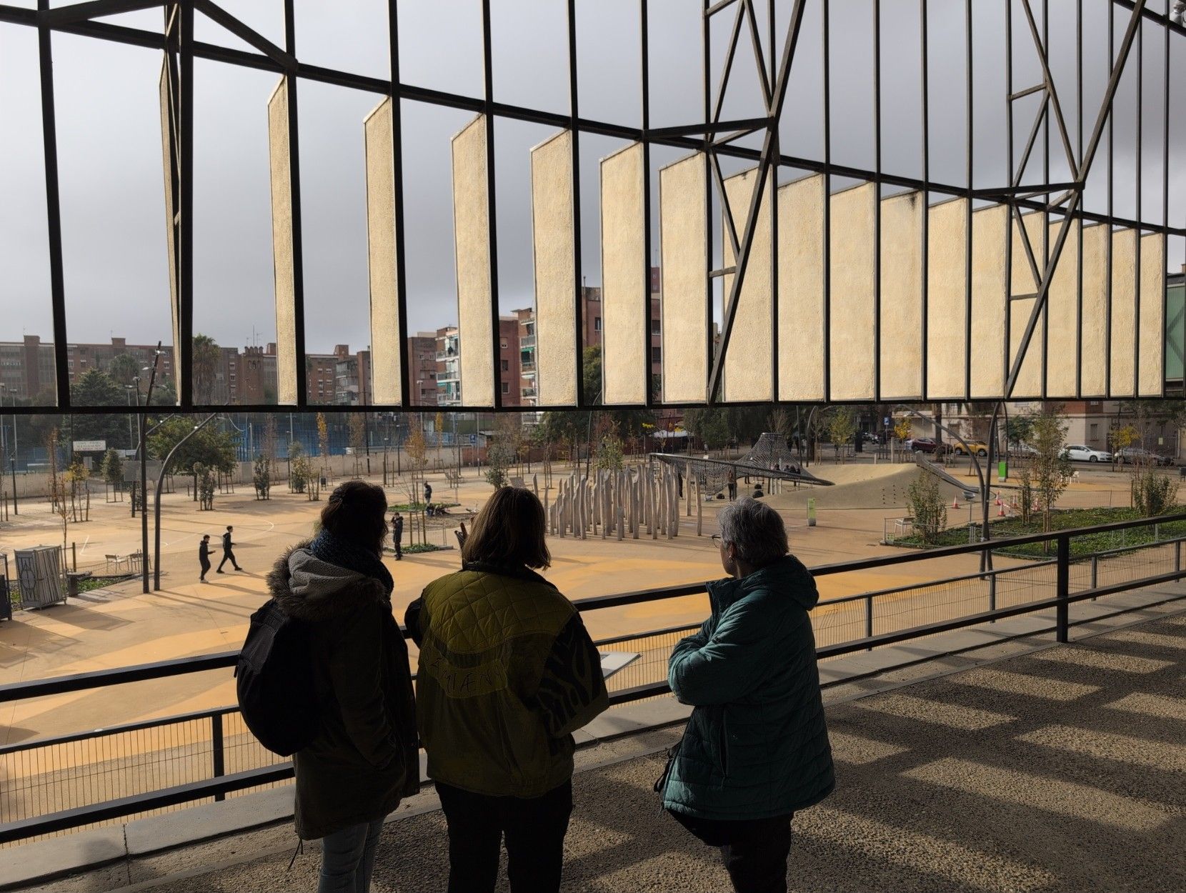 The back of three people (the two fellow attendees of our guided tour and our guide) looking at the square from the terrace of the Canodròm