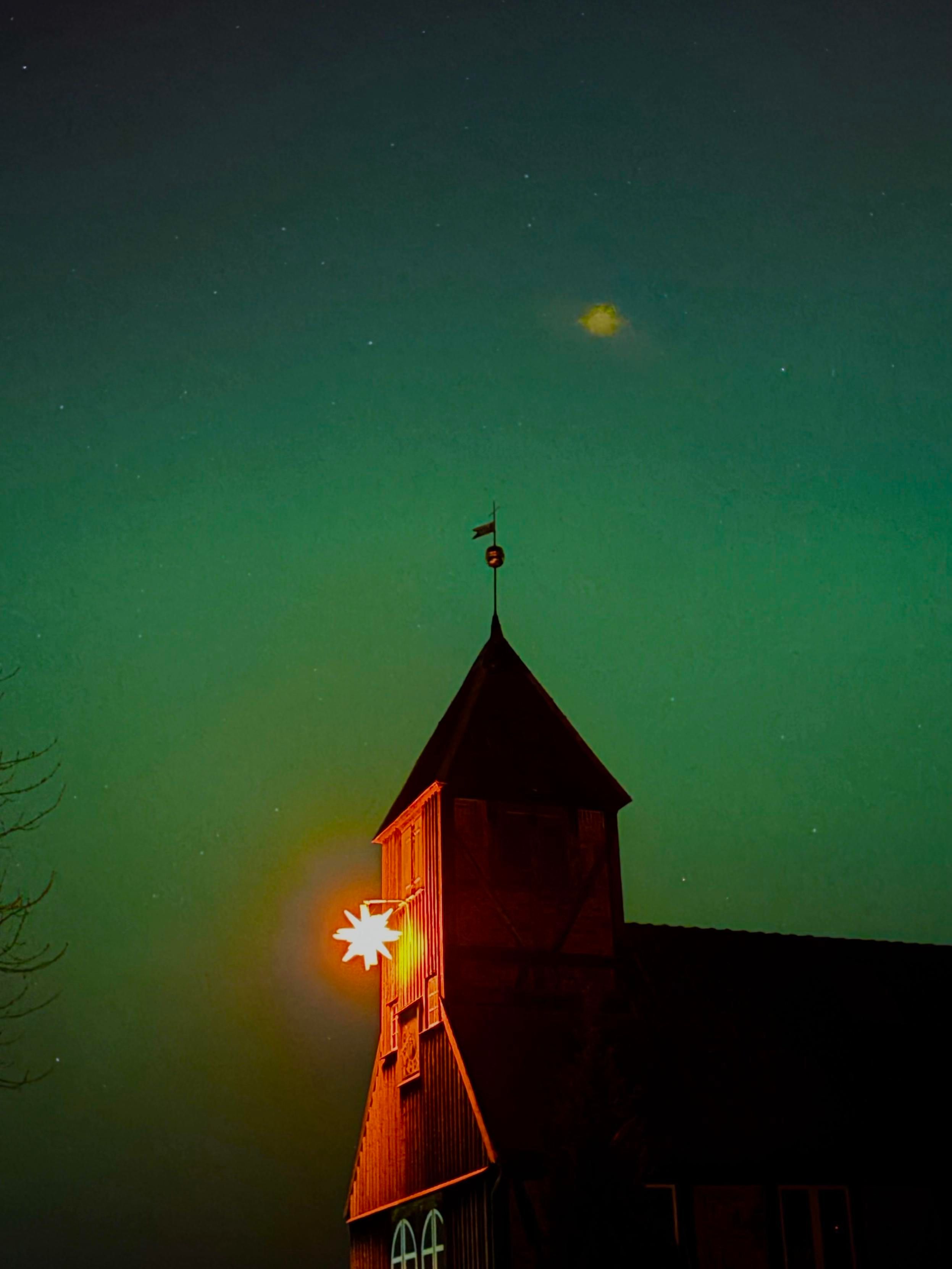 Eine Silhouette eines Kirchturms vor einem von grünen Polarlichtern beleuchteten Nachthimmel,