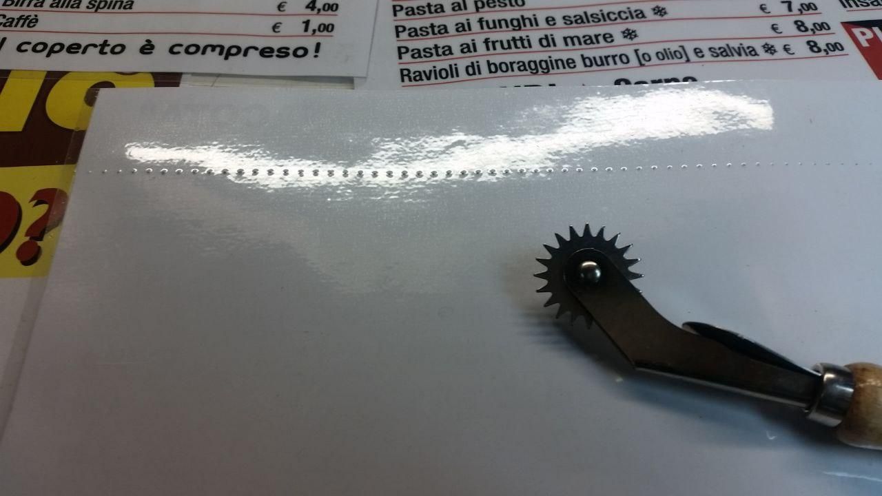 Fila di forellini intervallati di 4,30 mm sul retro di un foglio plastificato, con la rotella per sarti usata per farli.