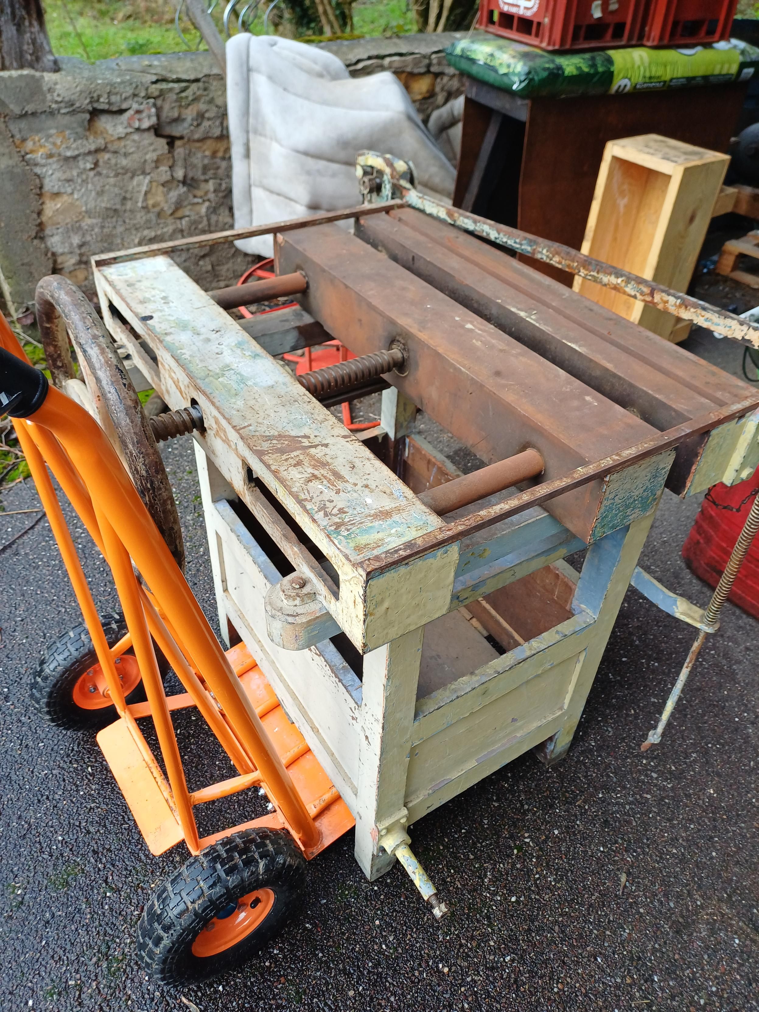Photo
Combiné à reliure, sur un diable orange.
La partie supérieure est en fonte rouillée avec une manivelle en fonte et une vis pour la partie mobile. Le piètement est en bois peint en gris-vert.