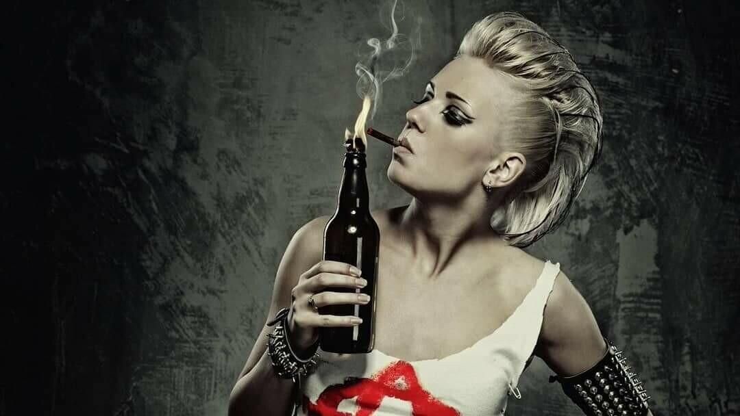 A blond woman with a fauxhawk, spiked armband, and ripped anarchy tee lights her cigarillo with a lit Molotov Cocktail. 