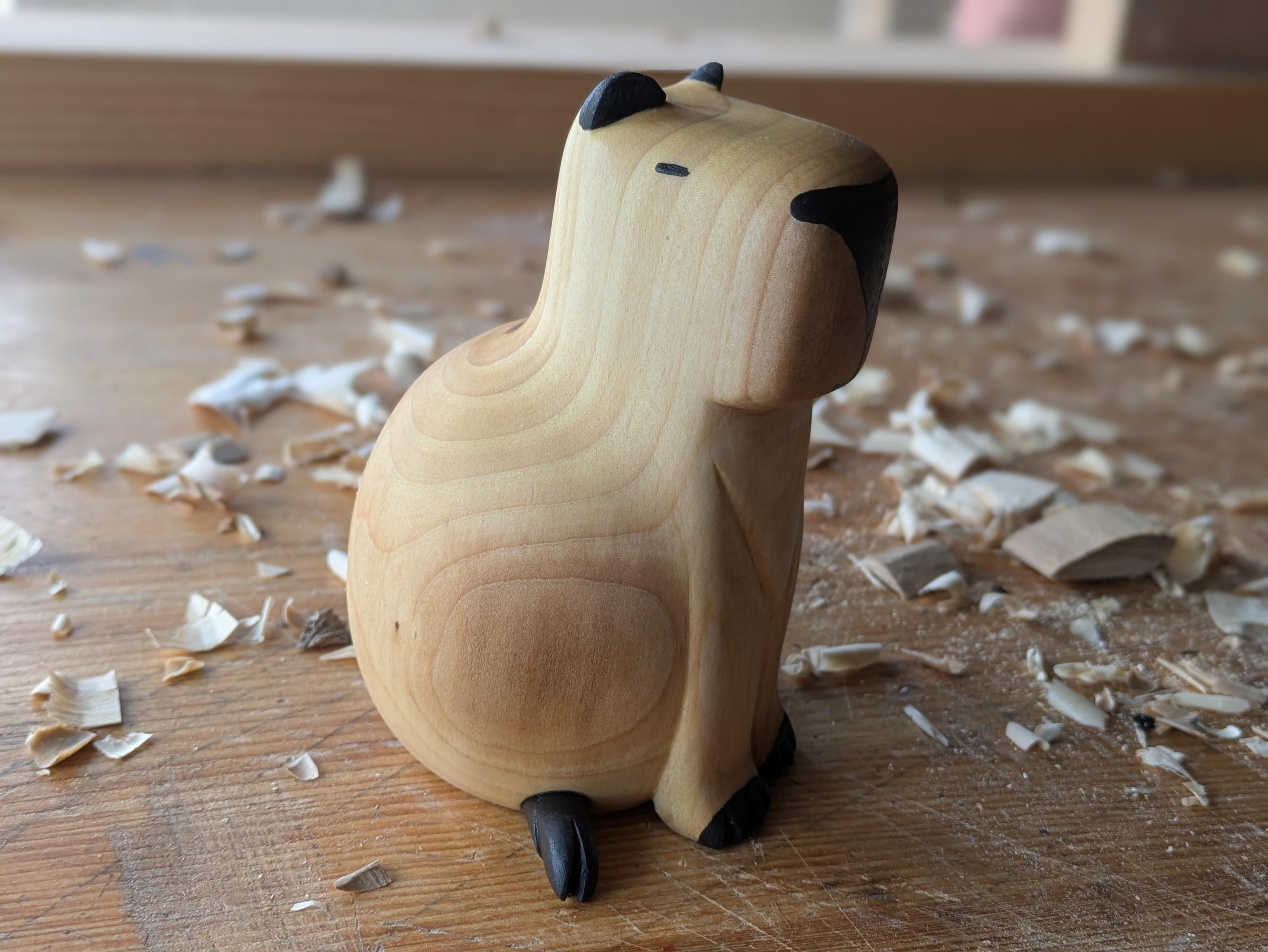 Woodcarved round capybara on a workbench woodchips around it.