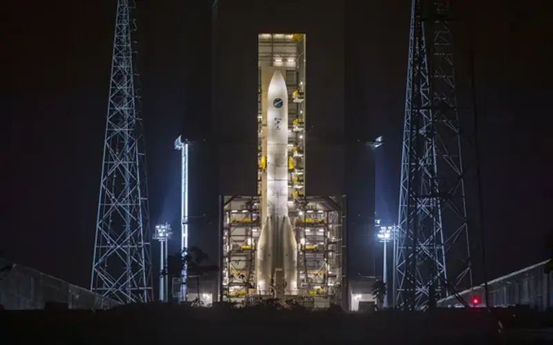 Ariane 6 visible de nuit sur son pas de tir, sous le portique mobile, éclairée par des projecteurs, entourée de structures métalliques antifoudre au Centre spatial guyanais. © ESA-CNES-Arianespace-ArianeGroup/Optique video du CSG S. Martin