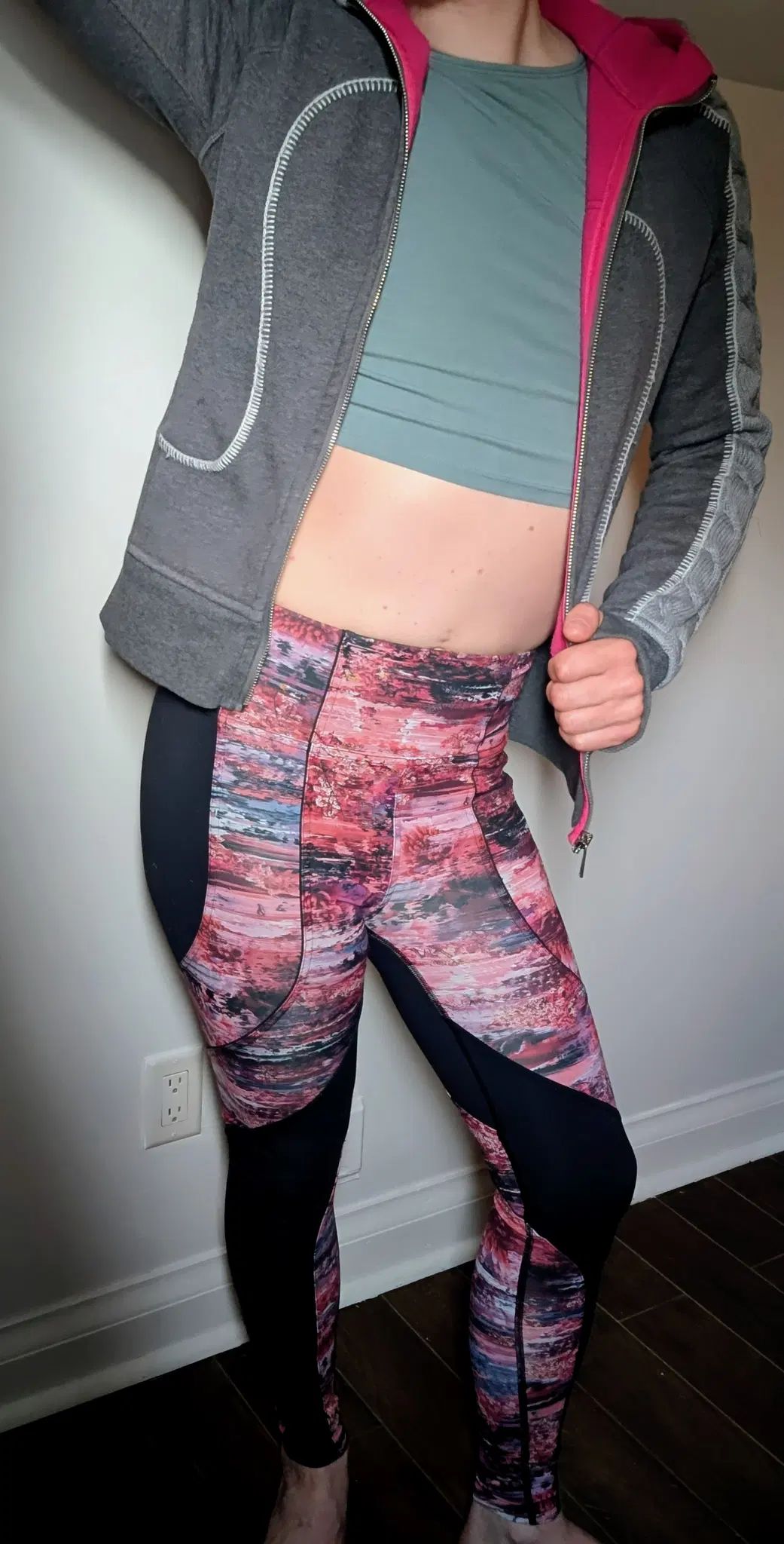 I stand in a fun pose, showing off my body in athletic clothes. My colourful leggings may hide my skin, but not my shape. I've unzipped my grey hoodie to let you view my tummy and tight green t-shirt. 
