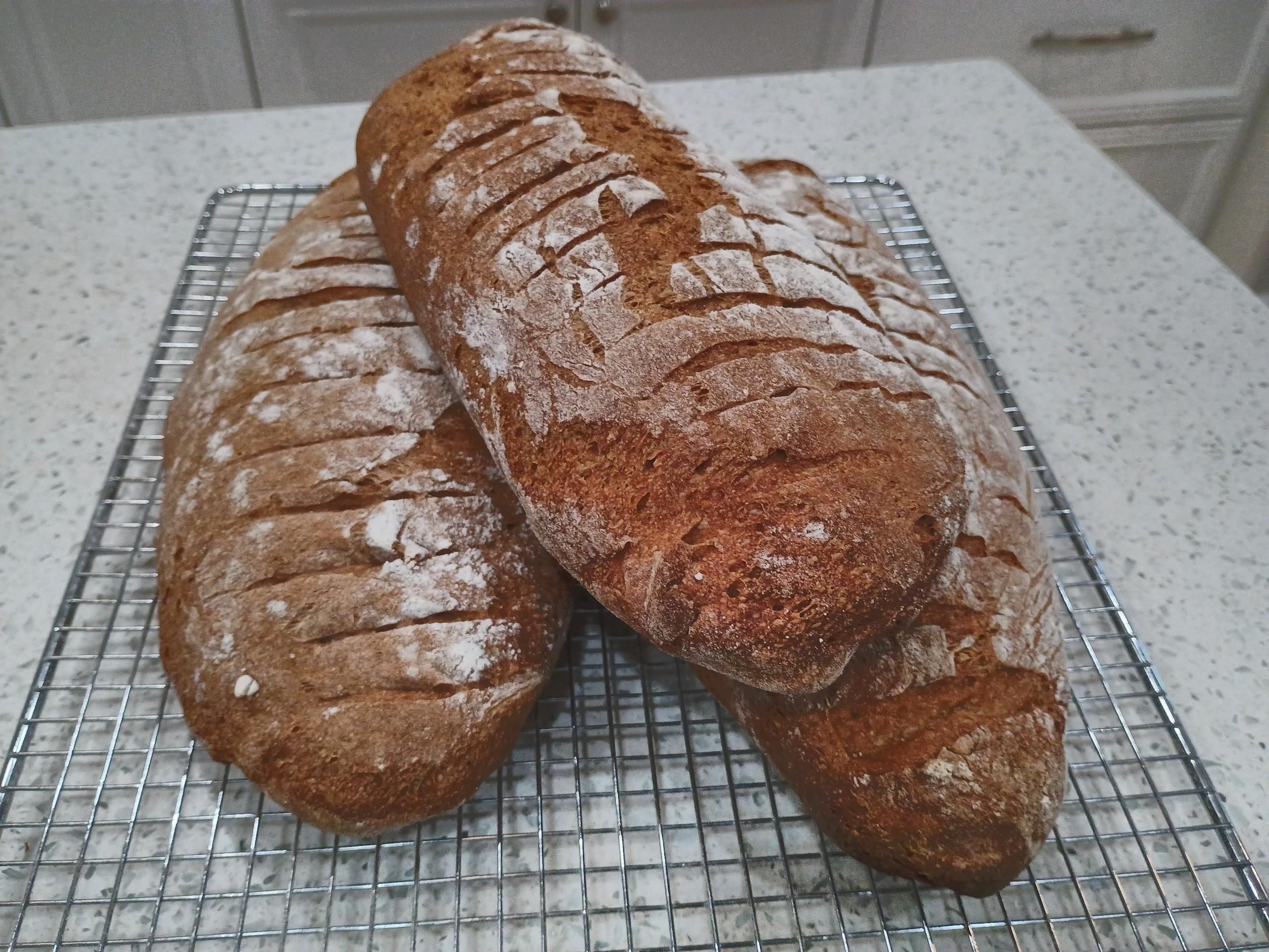 A stack of three deep-brown rye bread loaves. 