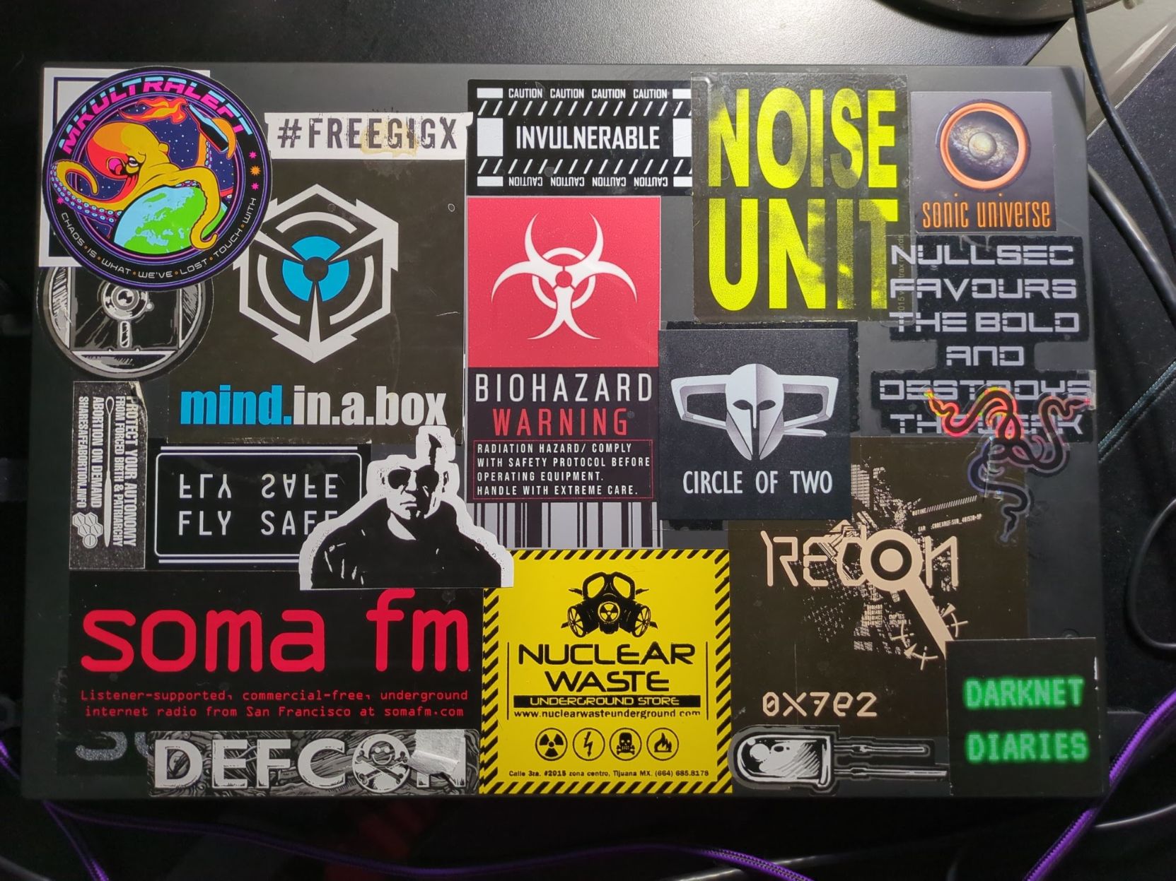 Black laptop with stickers related to underground music, EVE Online MMORPG (including banned legendary gigX, leader of Circle of Two corp that I was a member of back in the day), conferences including RECON, RE conference held in Montreal.