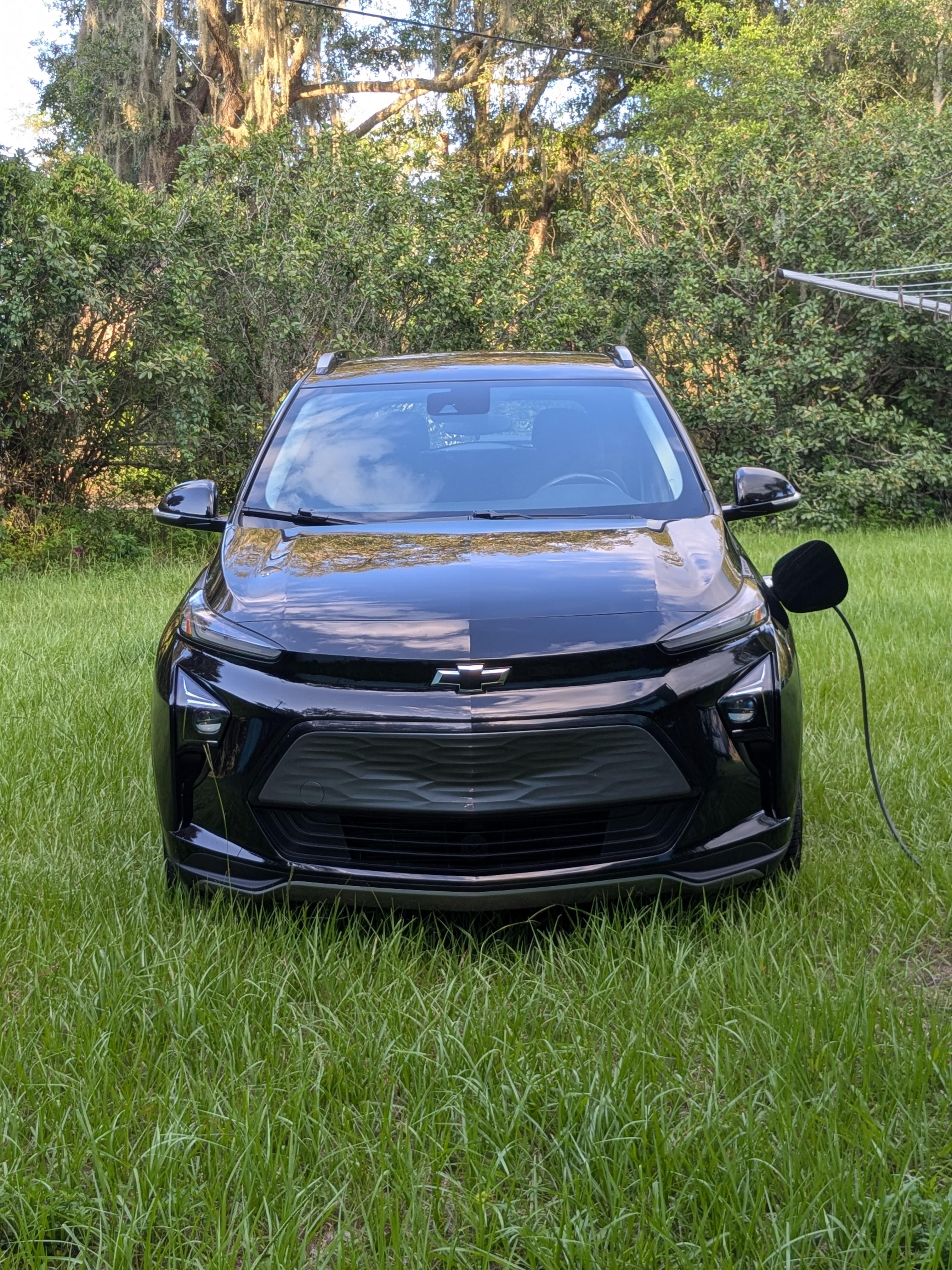 A black Chevy Bolt EV is charging in the sunshine on a green grassy lawn.