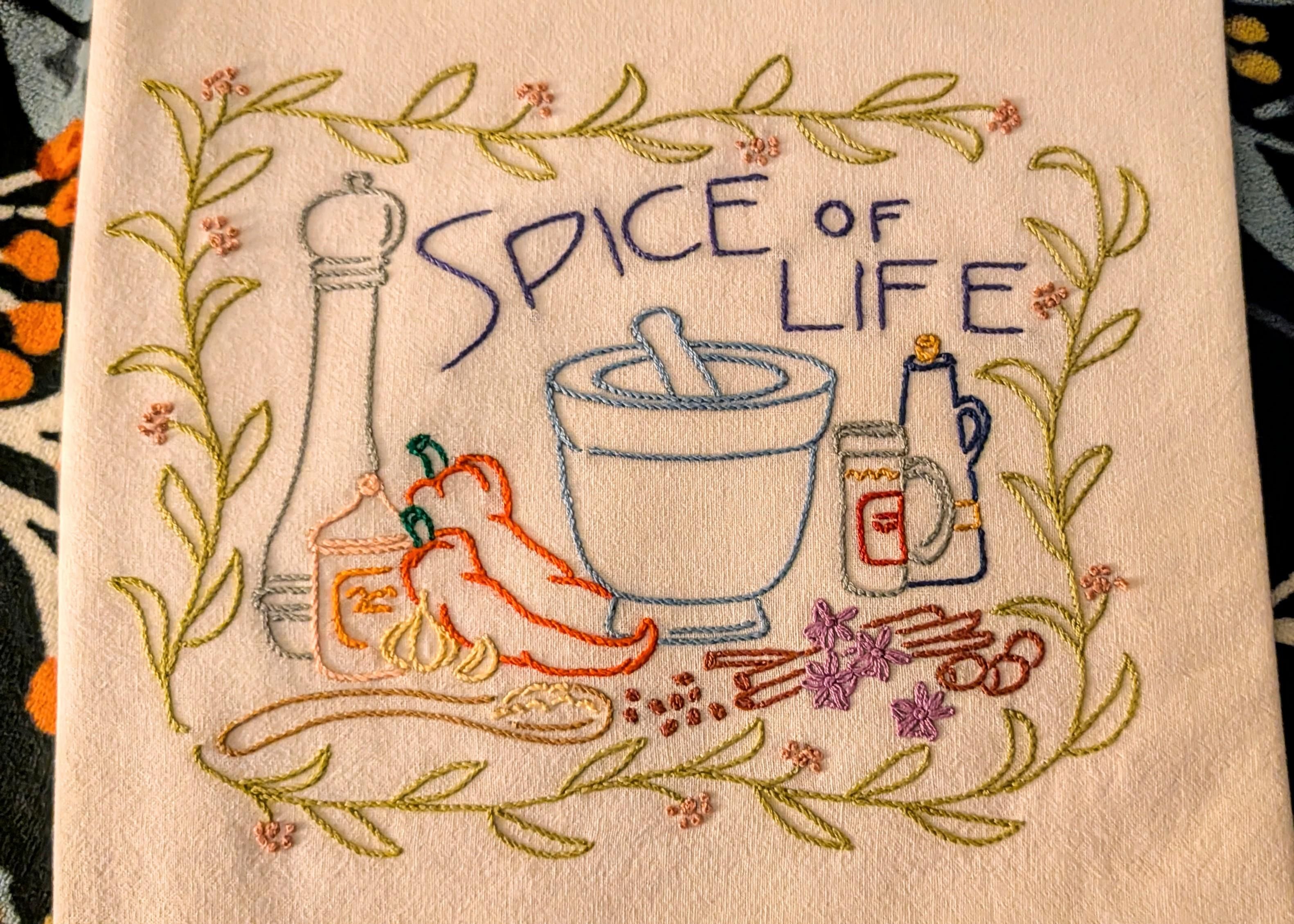 A colorful embridered flour sack dish towel. The theme is Spice of Life. 