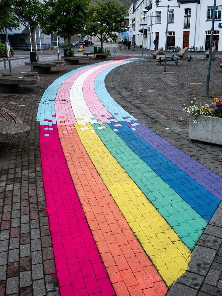 A brick walkway, painted as a rainbow path, which transitions to a path in trans colors.