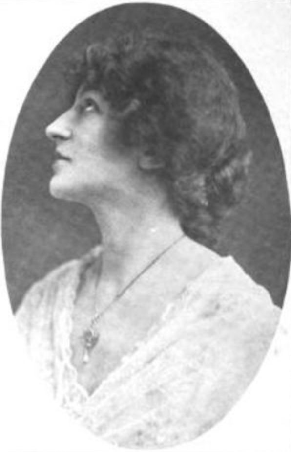 Edith Ostlere, a white woman with dark hair in a low bun, wearing a white lacy dress with a v-neckline 