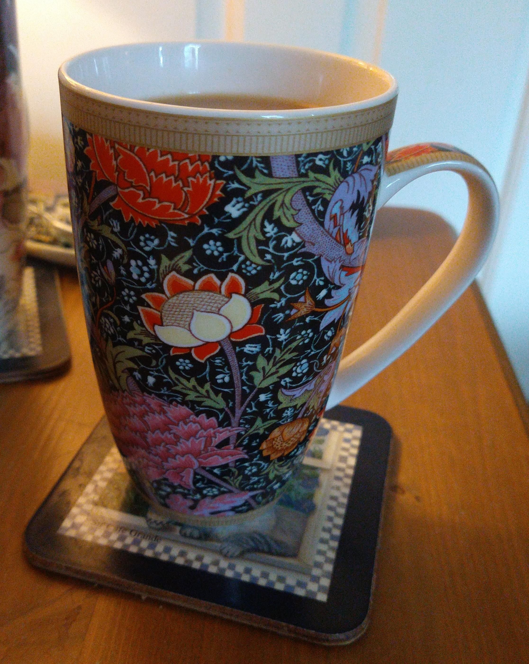 Mug of tea on a bedside cabinet with a William Morris pattern, of a dark background with floral design 