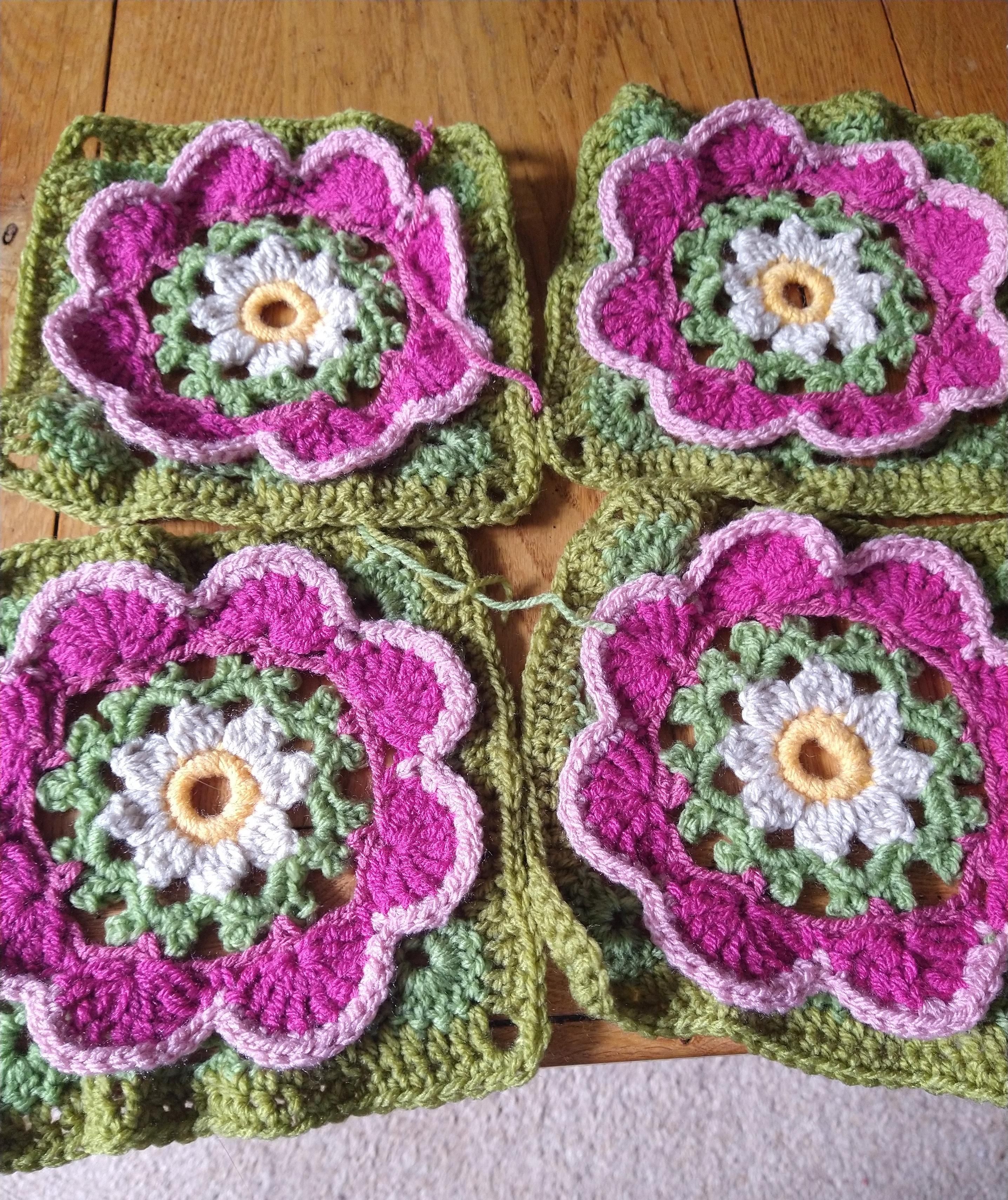 Four crochet flower motifs with pink flower shape centres and green borders 