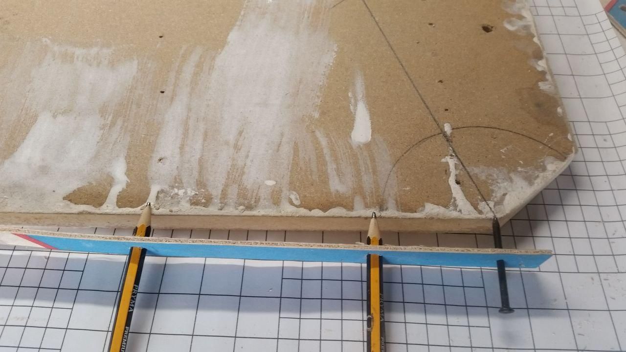 Una striscia di legno sottile, di dimensione qualsiasi, con un chiodo a un'estremità, per fare da fulcro, e due matite infilate a casaccio.
Con la matita più vicina al chiodo è già stato tracciato un arco con il centro in corrispondenza del vertice dell'angolo da dividere.