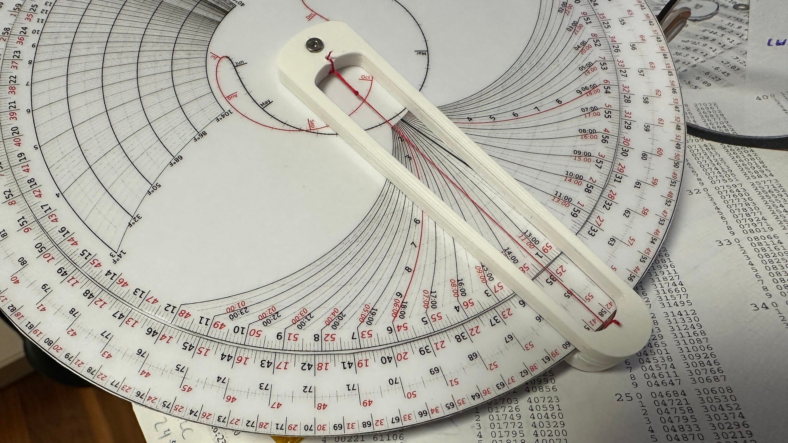 circular slide rule sitting on a table of numbers.  it has various nomograms for adjusting sextant measurements