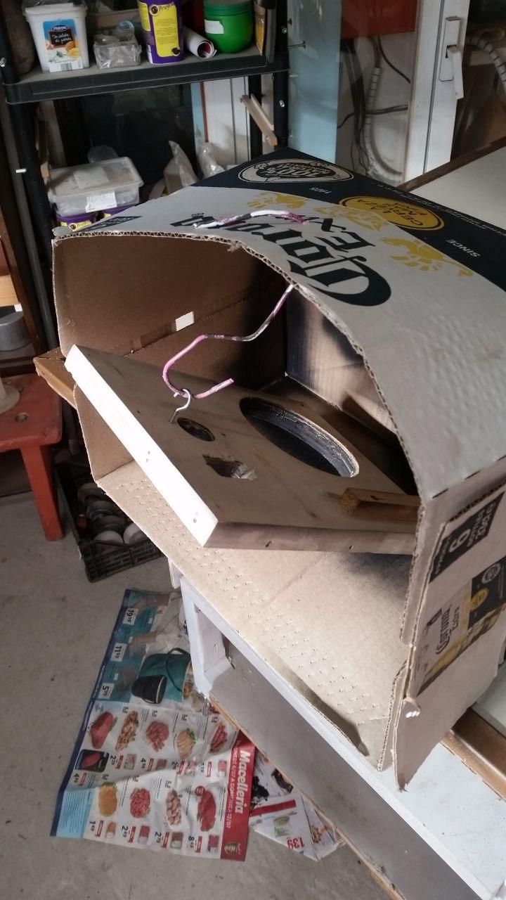 Scatola di birra Corona con un gancio in filo di ferro al quale è appeso un pezzo di compensato da finire di pitturare a spray.