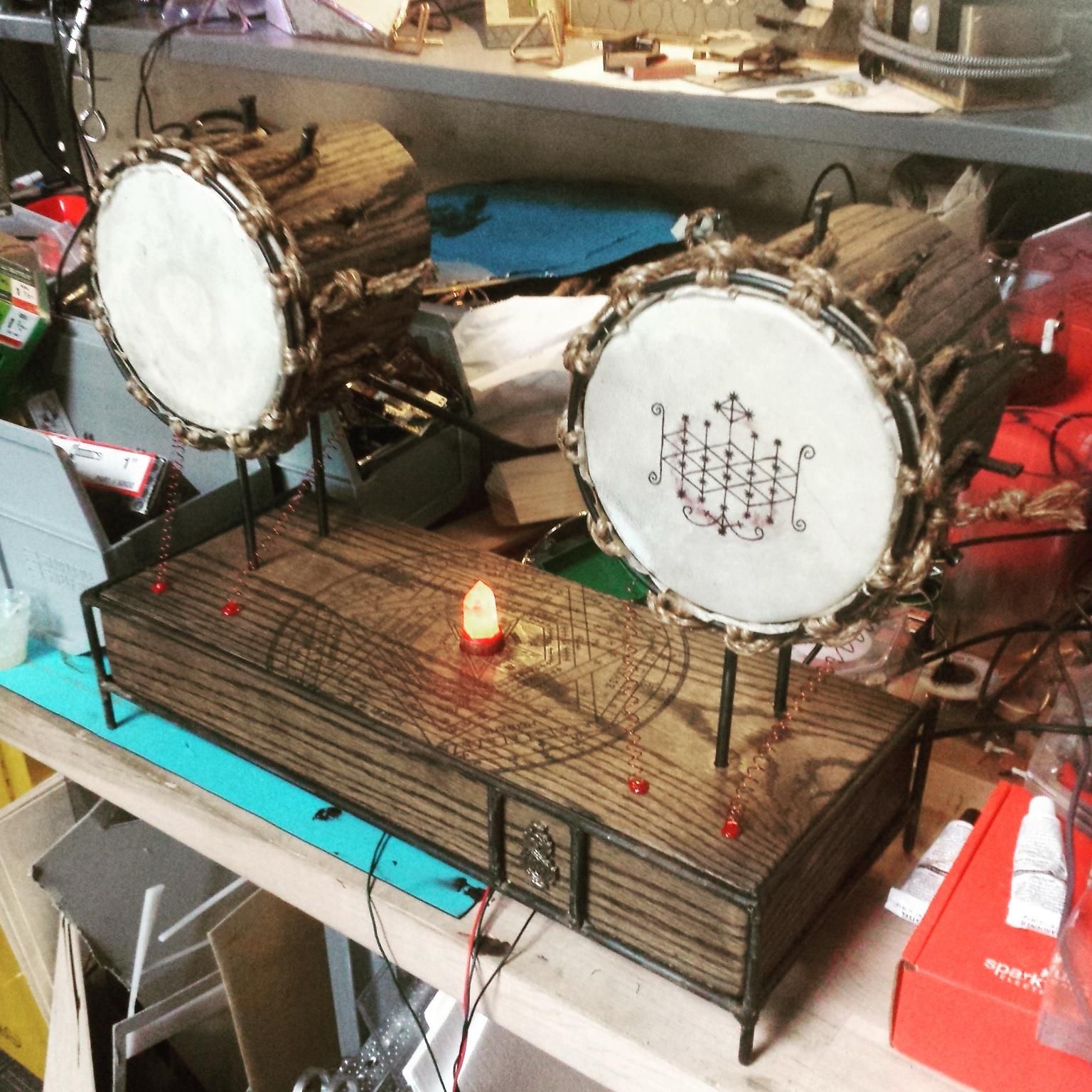 Close-up of the stereo shelf-system. Two round speakers on steel legs are connected to a central wooden box with a steel frame. 