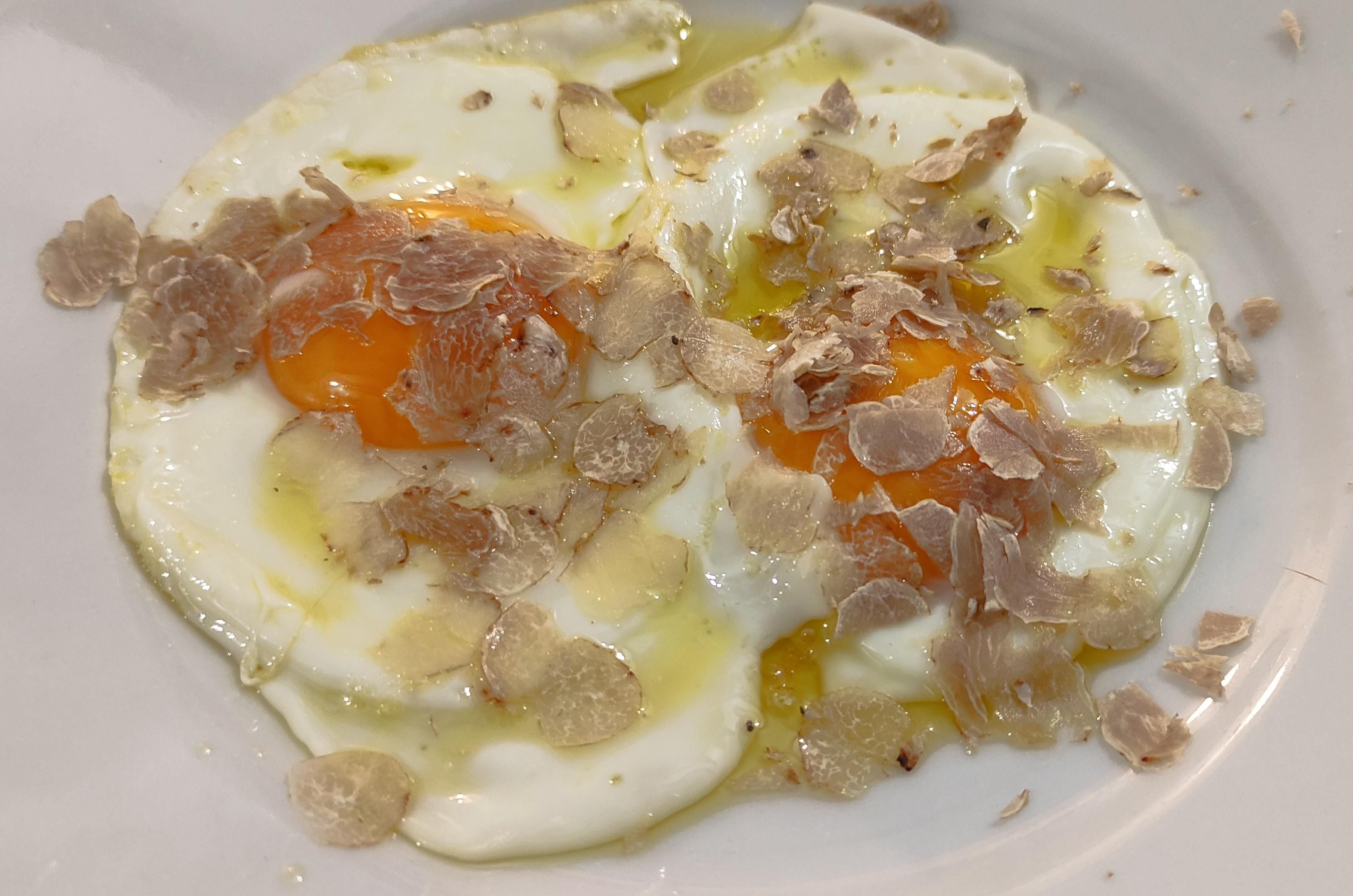 due uova al tegamino ricoperte di tartufo su un piatto di ceramica bianca 