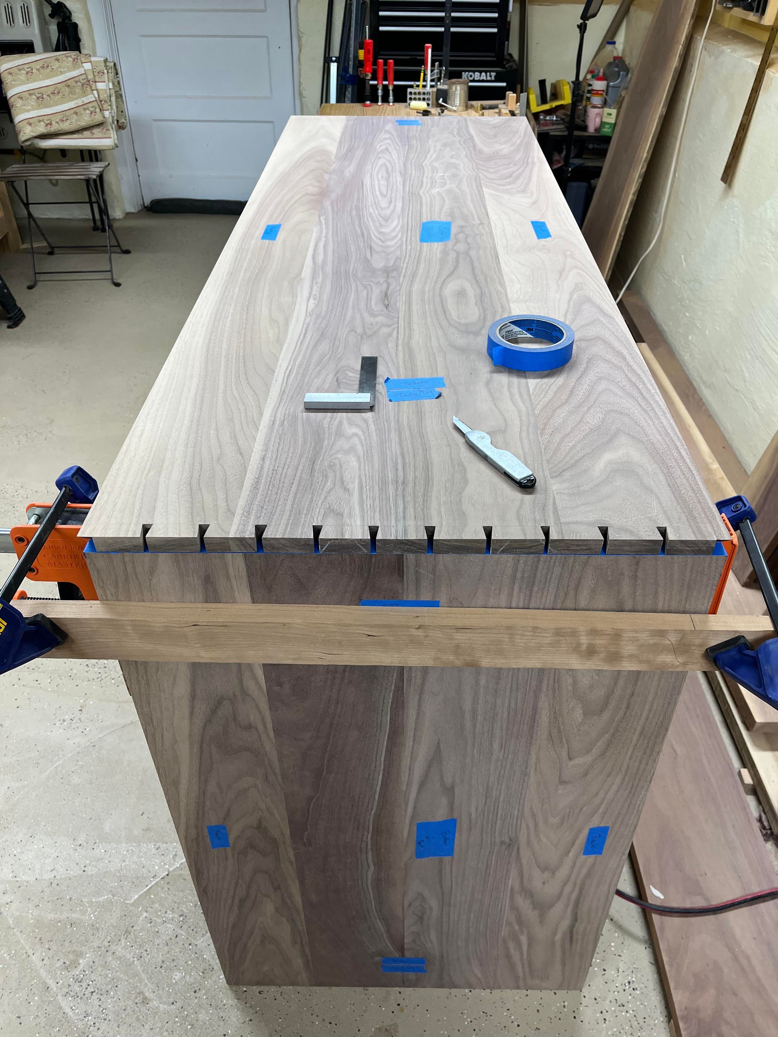 Two walnut boards meeting at a 90 degree angle. The top board has dovetails that will be transfered to the board below it.