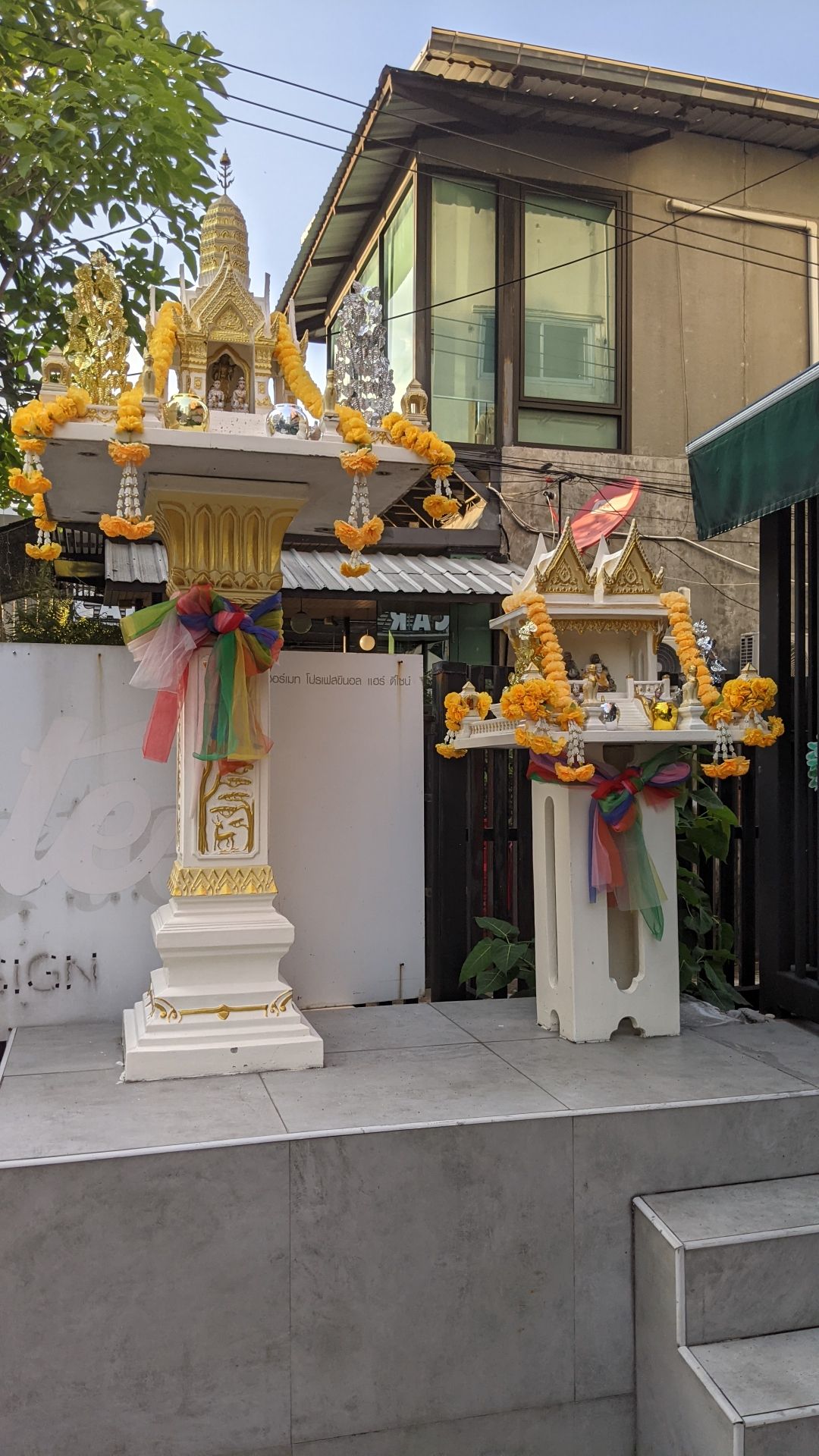 Two spirit houses outside a cafe. They're white and gold mini-temples on pedestals, lots of Thai buildings have them.