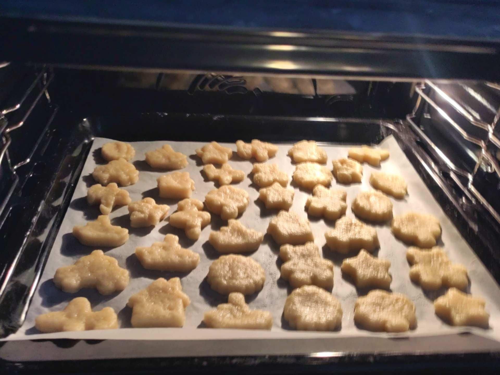 Teglia di biscotti crudi in forno. I biscotti hanno varie forme: stella, aeroplano, macchinina, casetta...