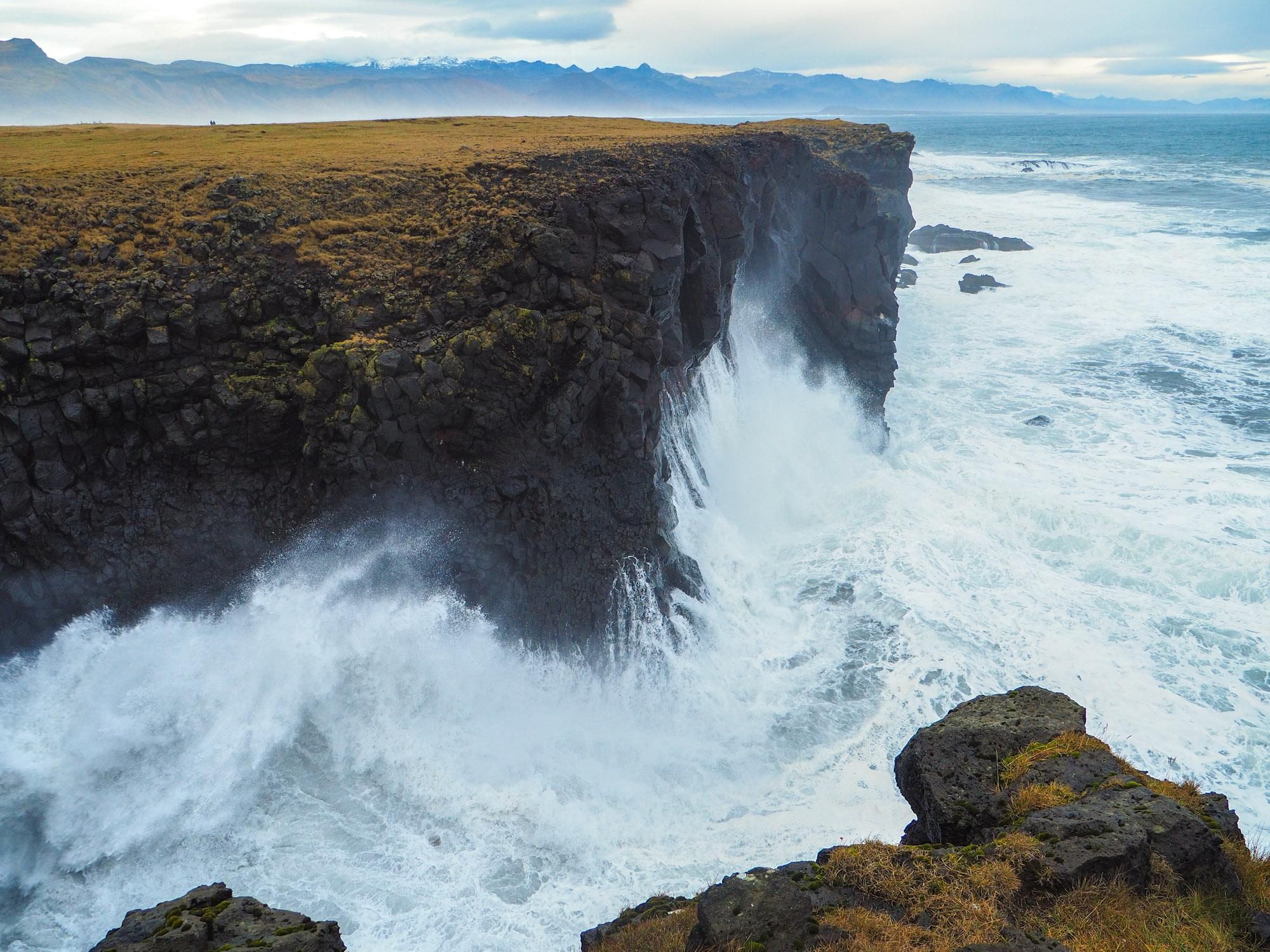 Big waves crashing against black sea cliffs on a moody day. 